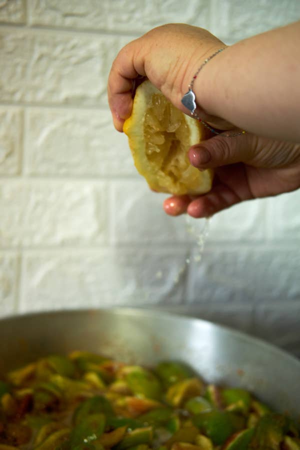 A hand squeezes a lemon over a pan of cooking fruits or vegetables, adding freshness to the dish