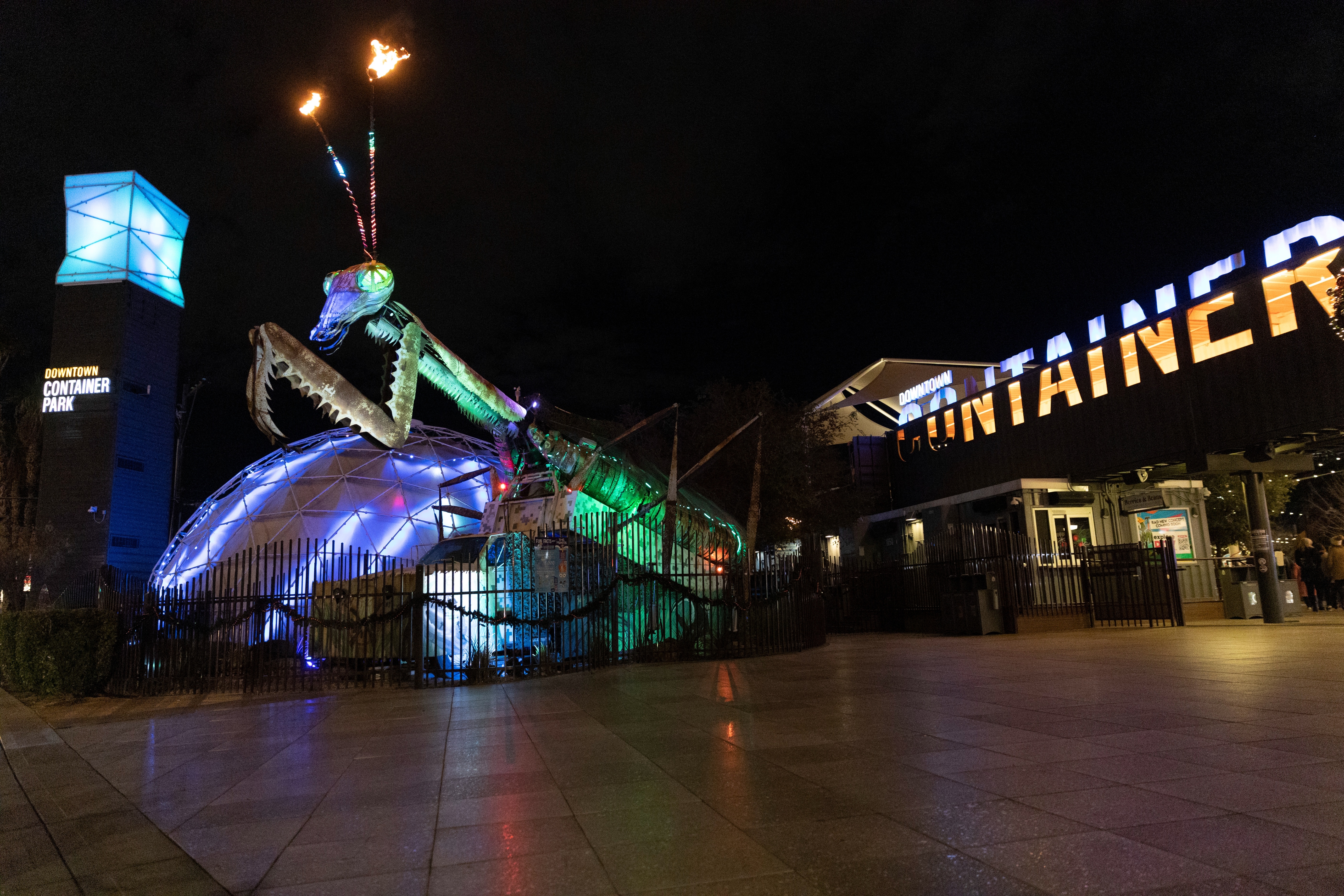 Giant, illuminated praying mantis sculpture with fire-breathing antennae outside Downtown Container Park at night