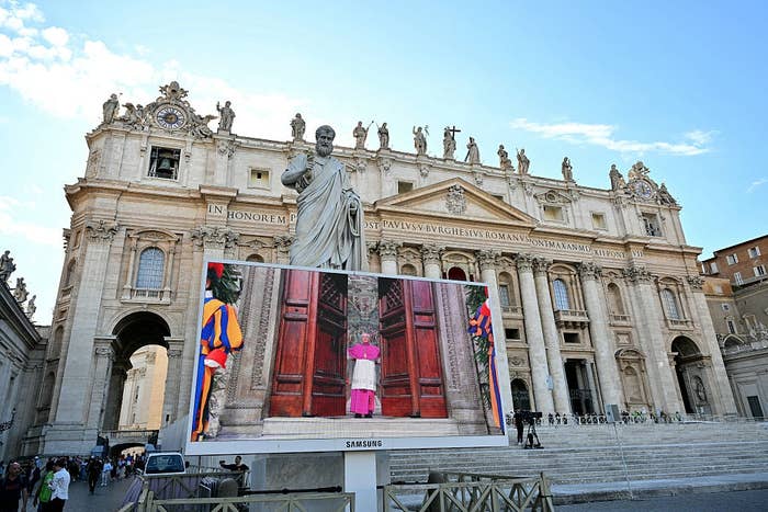 A Samsung screen displays a person dressed like the Pope, wearing a magenta robe, humorously placed before the doors of a grand historic cathedral