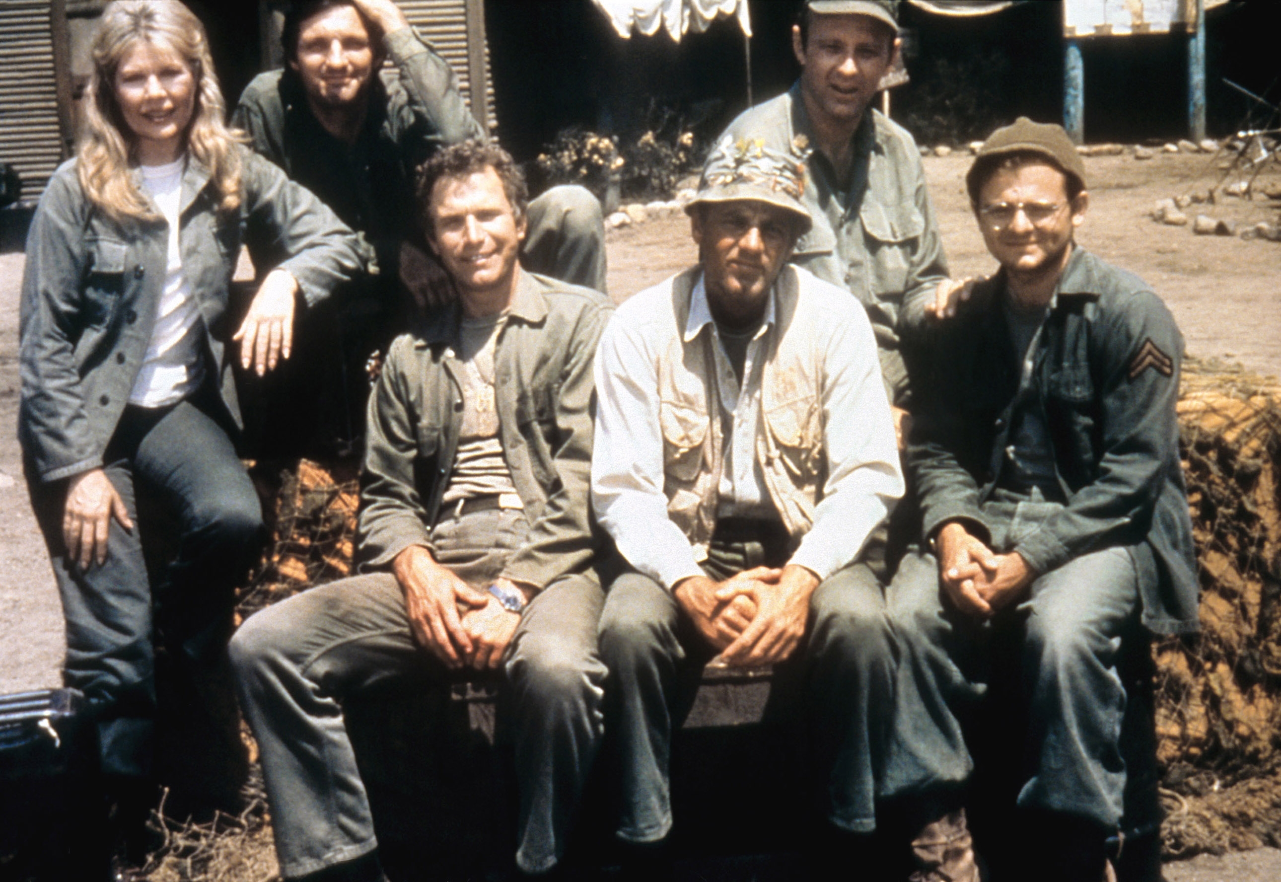 Cast of a classic TV series posing outdoors in casual, military-style clothing