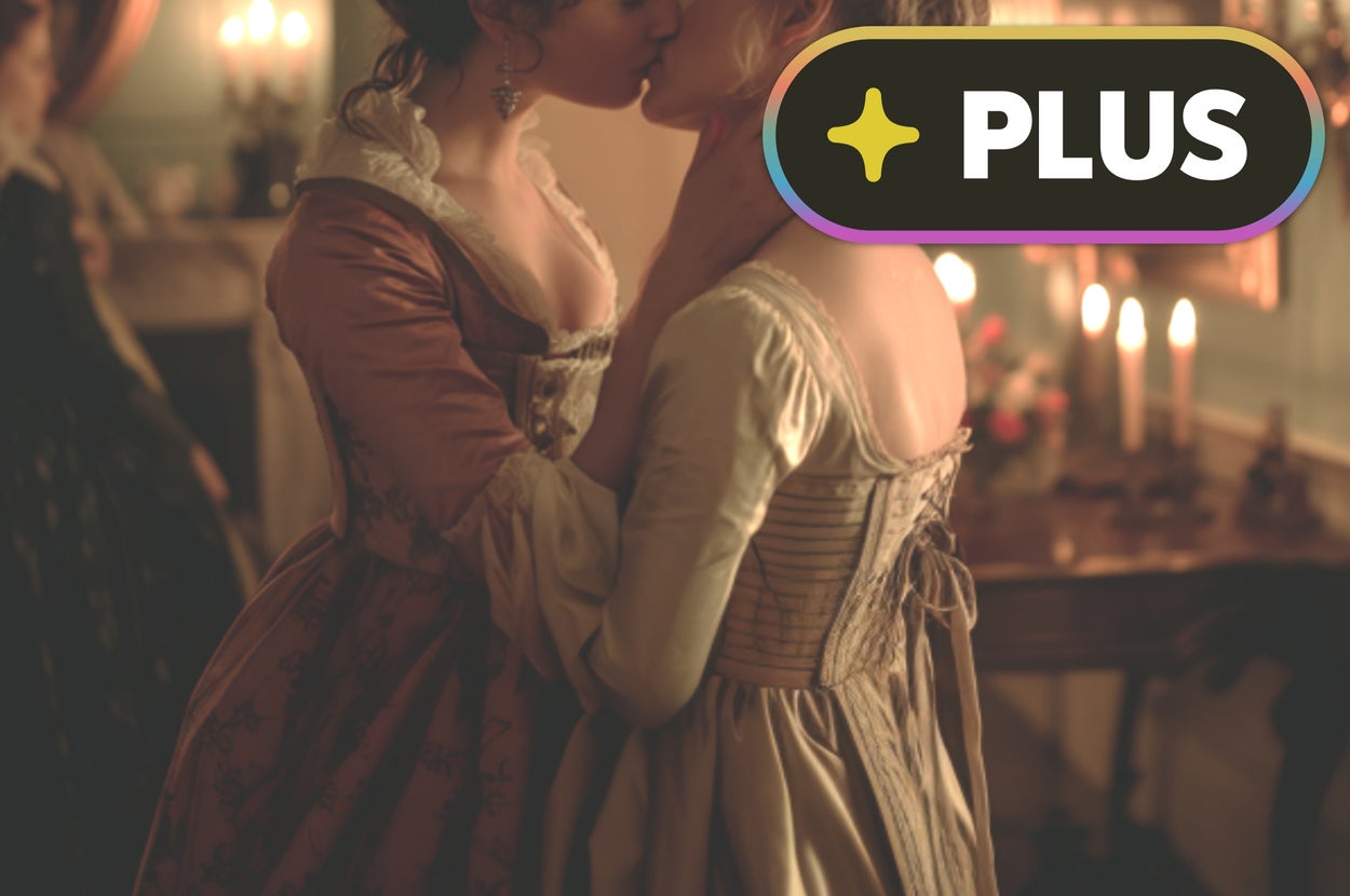 Two women in 18th-century-style dresses share an intimate moment in a candlelit room, evoking a historical or literary theme