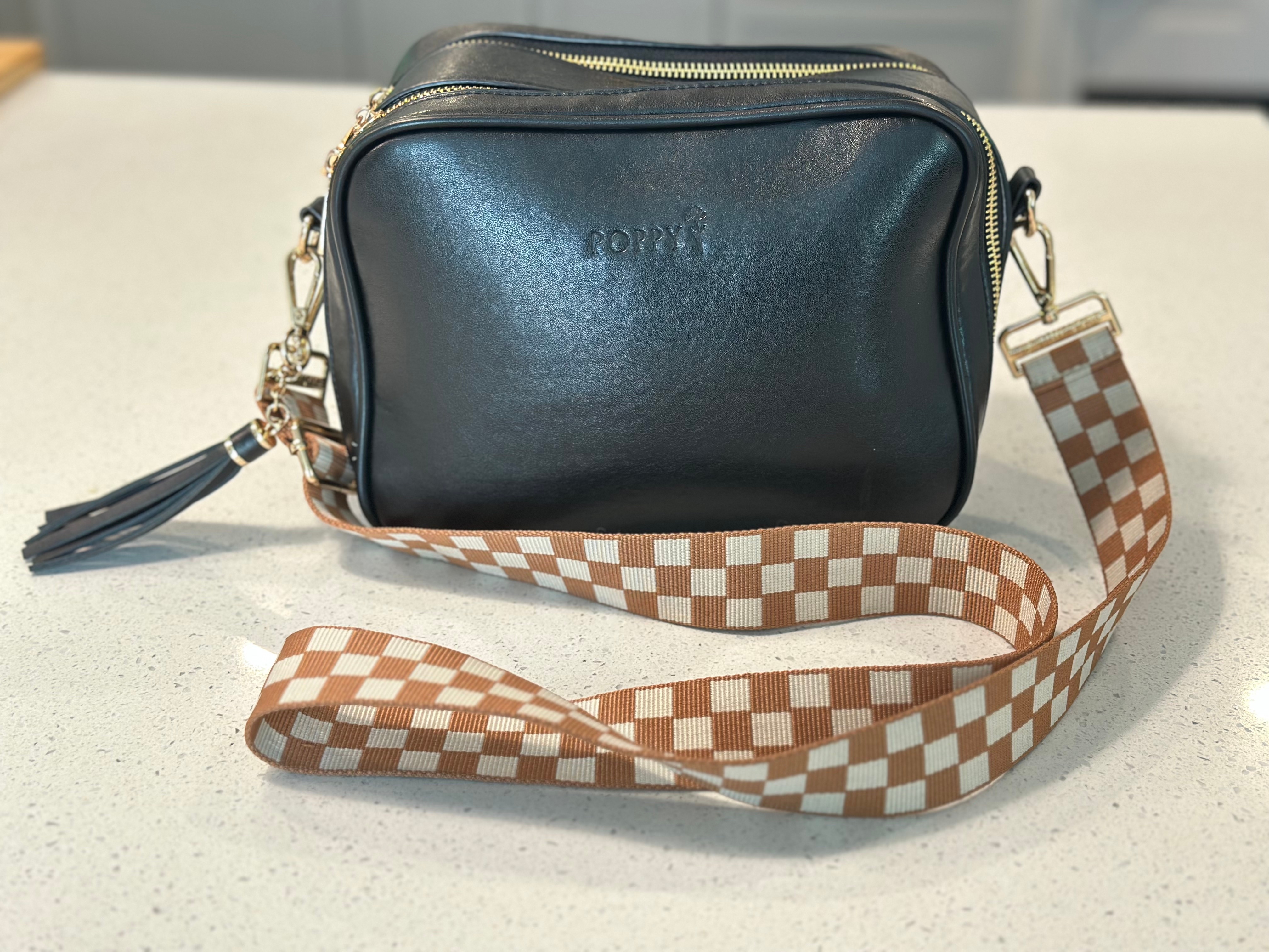 Stylish rectangular leather bag with embossed word and tasseled zipper, featuring a checkered adjustable strap on a countertop