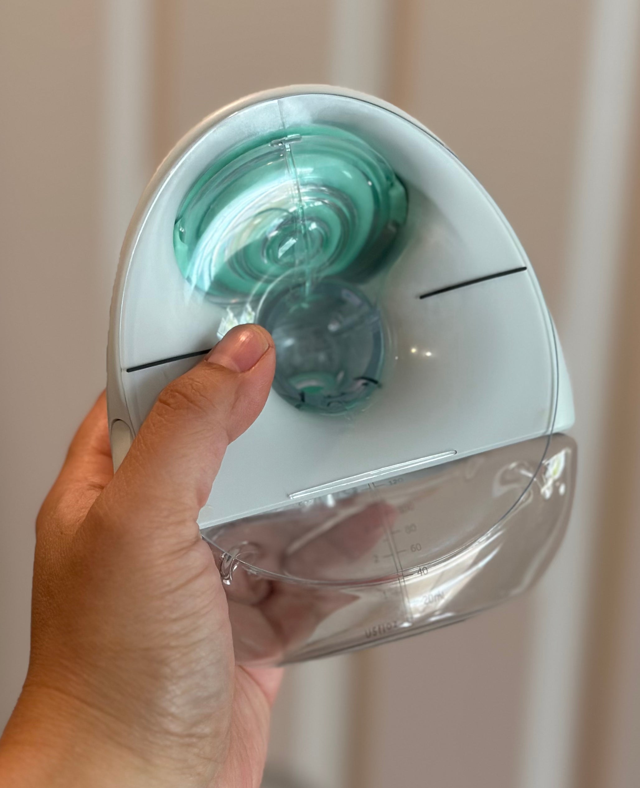 Hand holding a small, modern pump with a clear water reservoir in front of a door