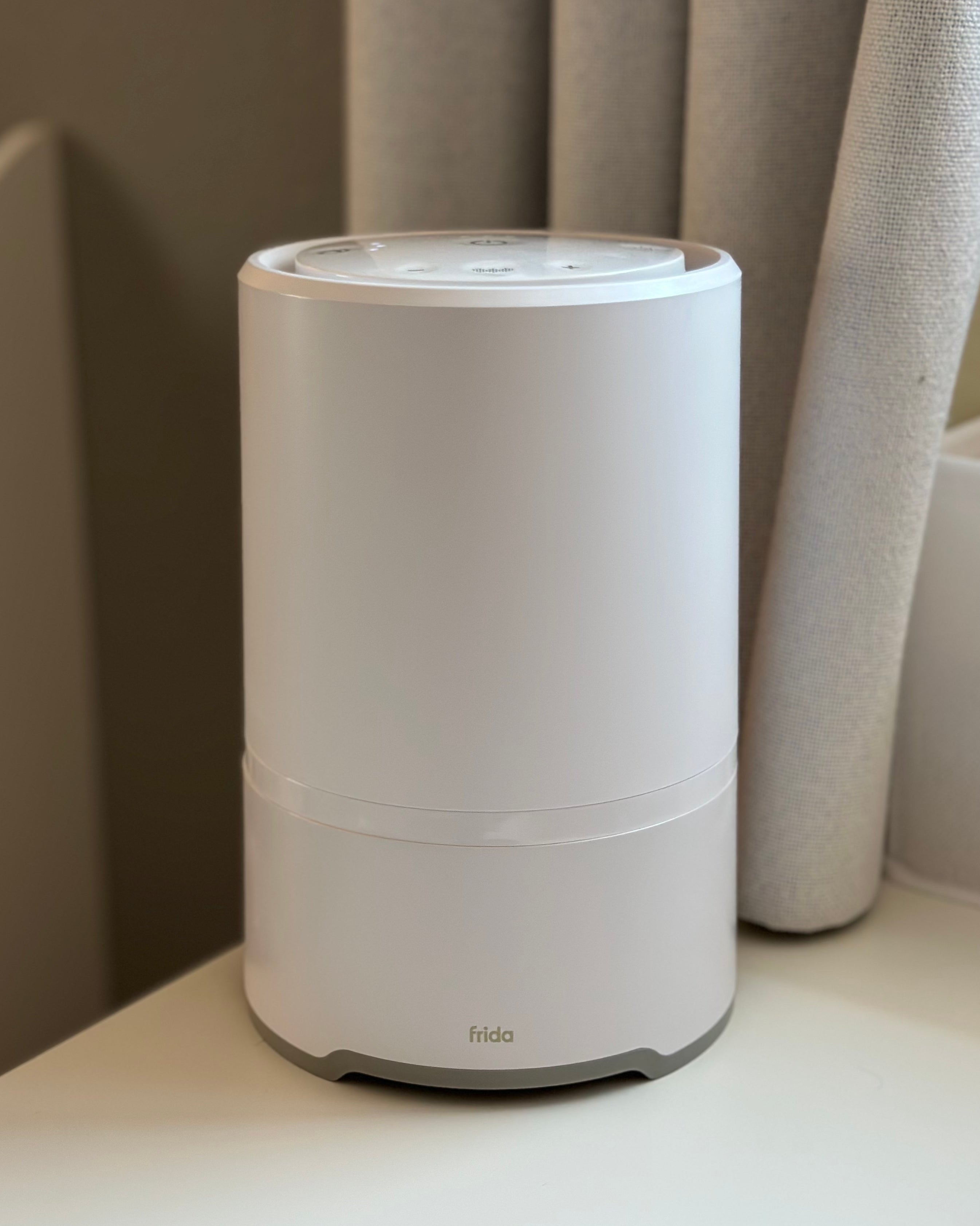 A cylindrical, white air purifier on a table next to light-colored curtains