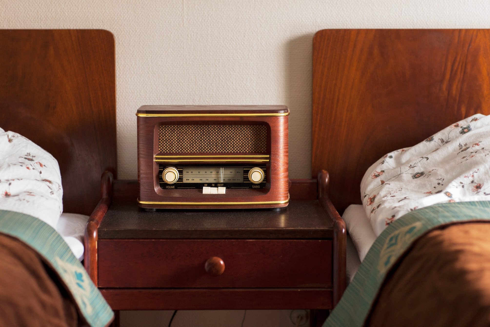 Vintage radio on a wooden bedside table between two beds with patterned sheets