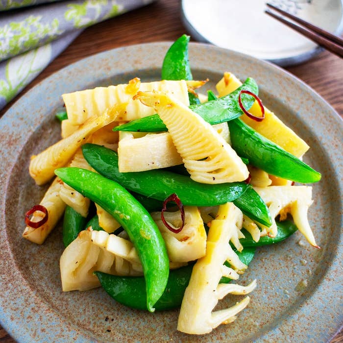 皿に盛られたサヤエンドウとタケノコの炒め物。シンプルで健康的な料理がテーブルに置かれている。