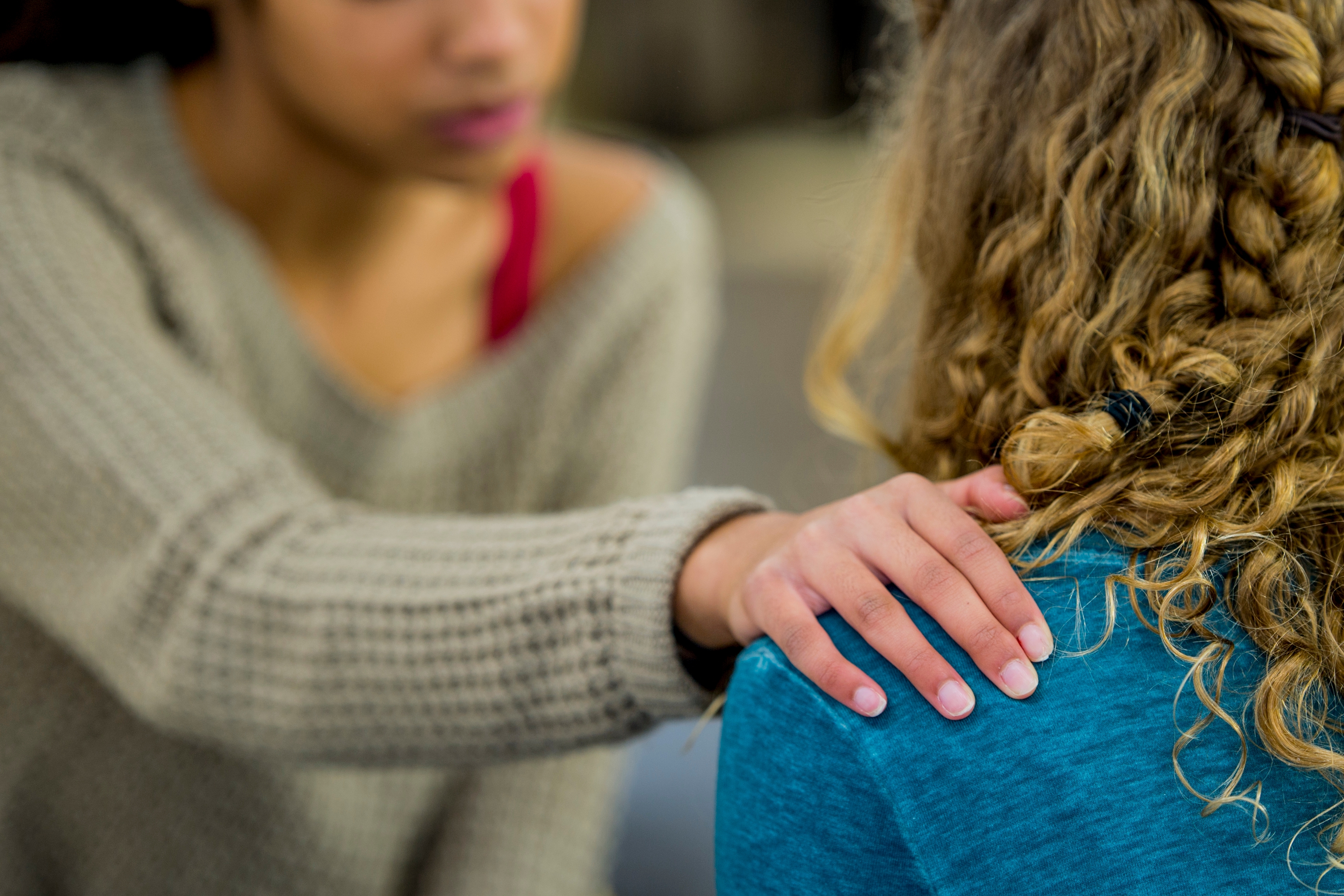 Person offering comfort by gently patting another person's shoulder, suggesting empathy and support in a moment of need