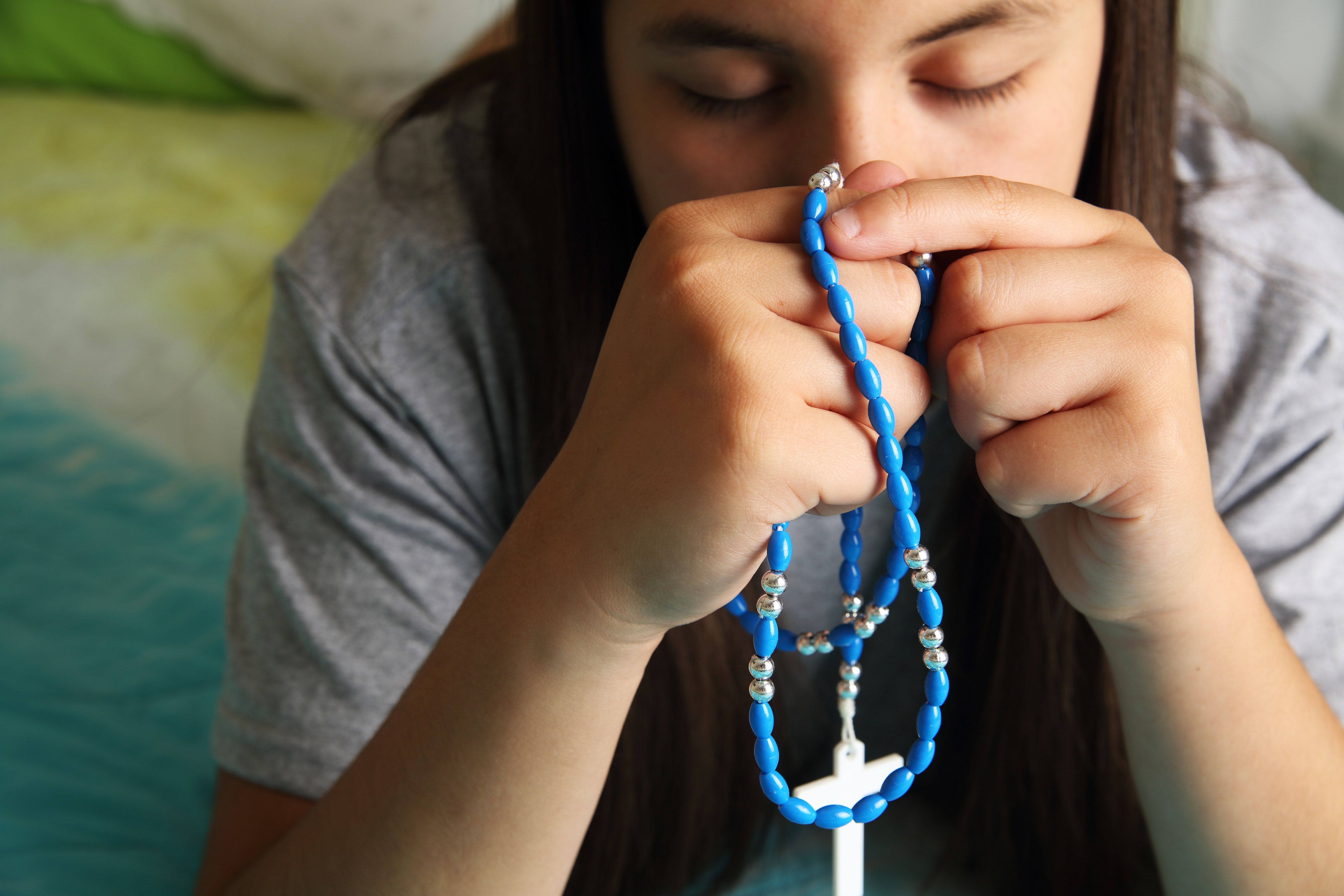 Person holding rosary beads in prayerful pose
