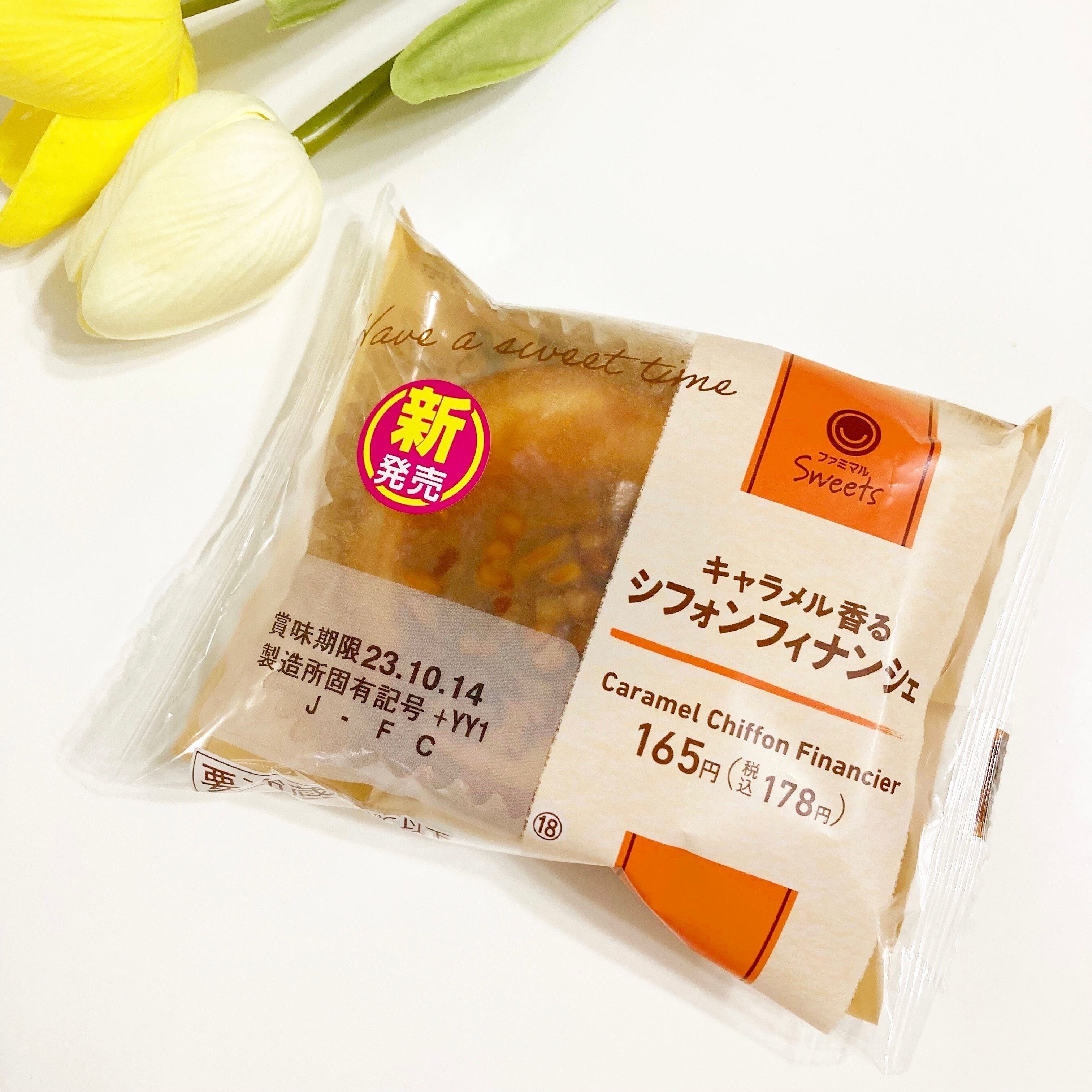 キャラメルシフォンフィナンシェの包装。価格は165円(税別)。発売中で、新発売マーク付き。背景にチューリップが見える。