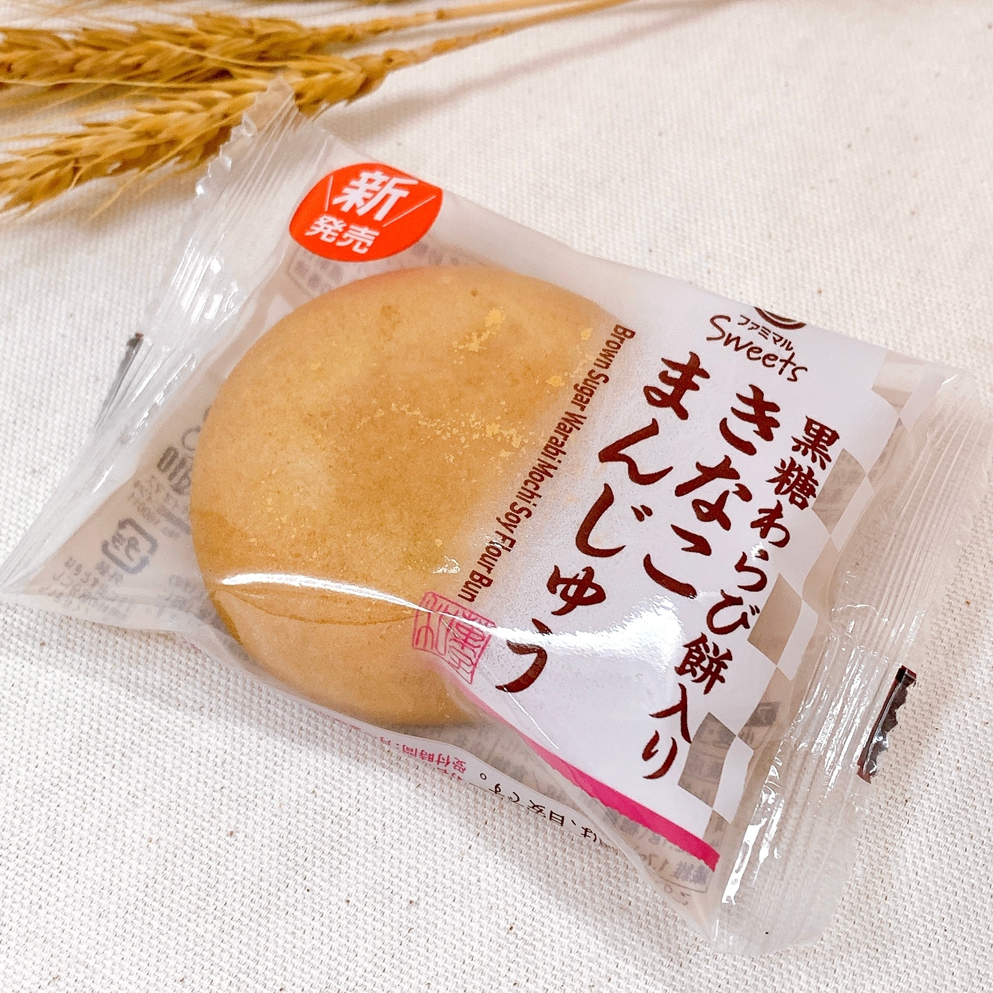 包装されたきなこ餅入りまんじゅうが布の上に置かれ、横には穂が添えられています。