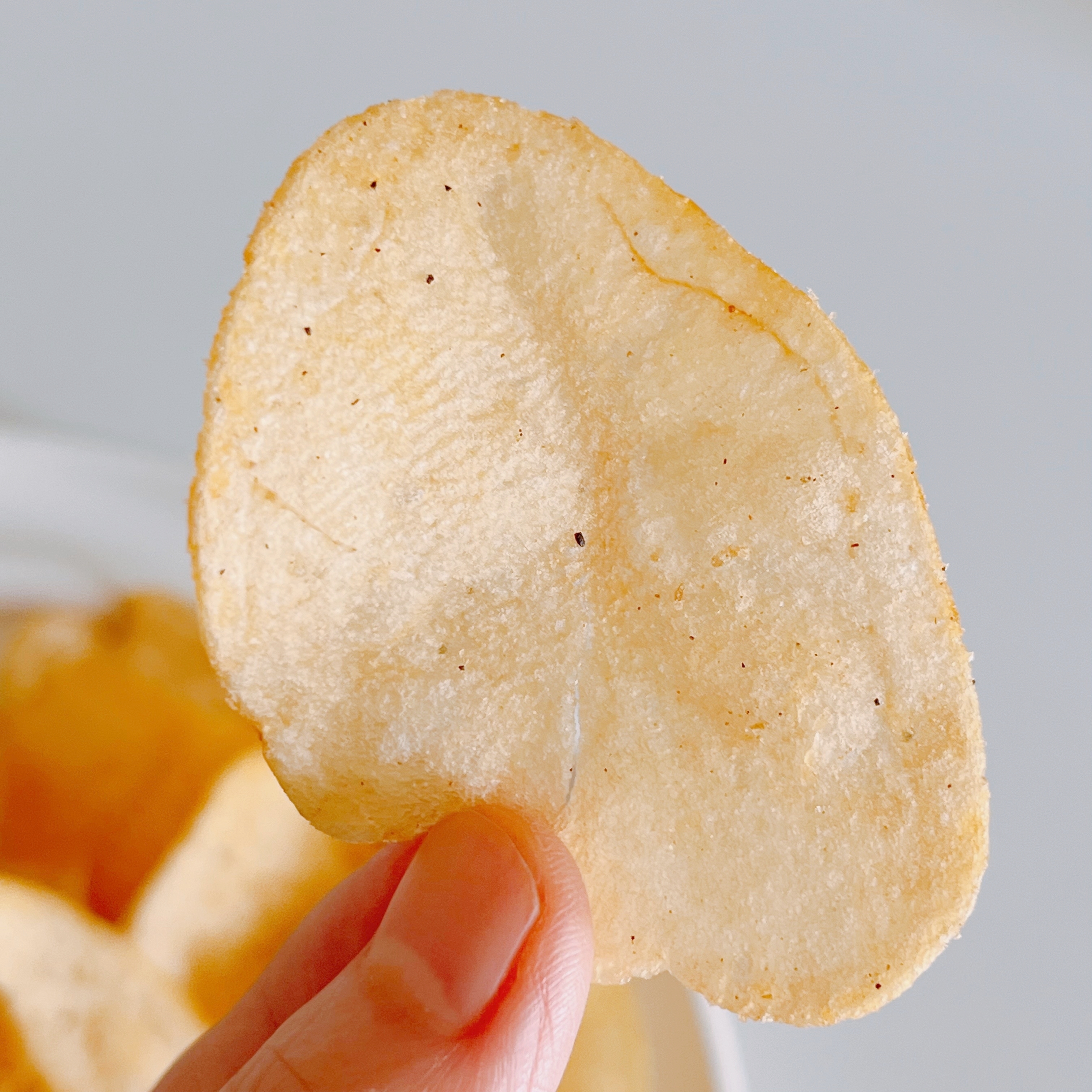 手に持たれたポテトチップスのクローズアップ。サクサクした質感が感じられる。