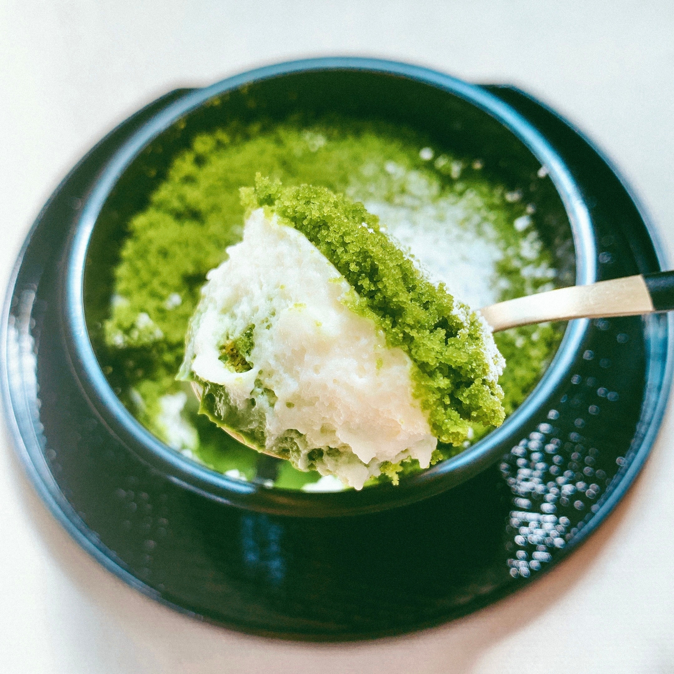 スプーンが抹茶パフェをすくっている様子。クリーミーな白い層の上に抹茶の層。