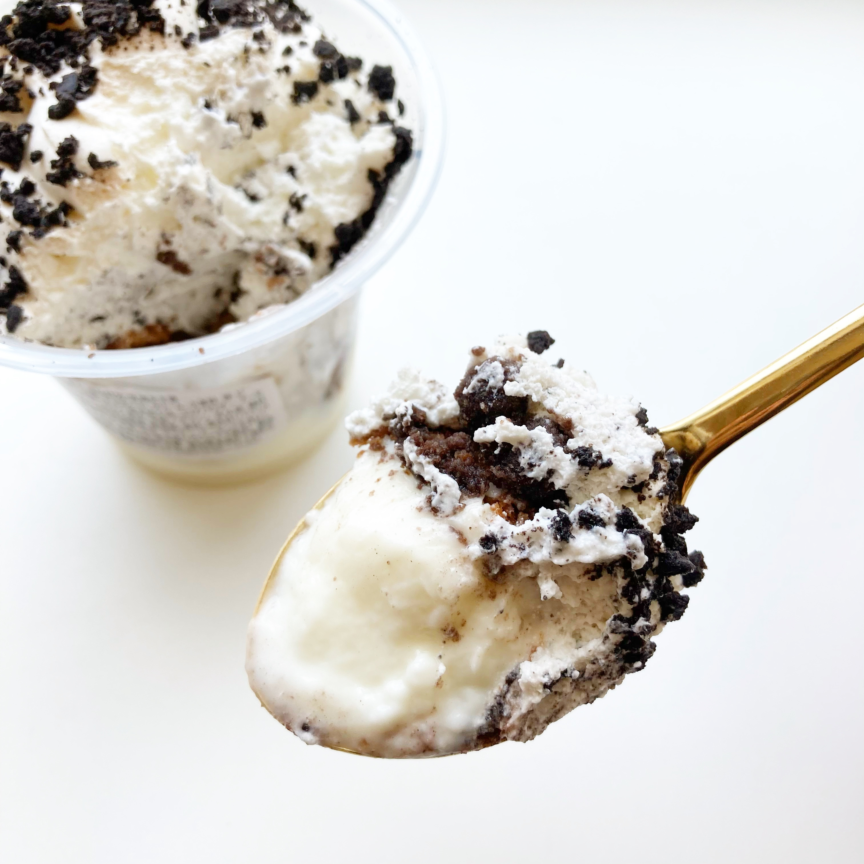 カップのアイスクリームの上に、小さなチョコレートクランチがトッピングされている。スプーンに一口分がすくわれている。