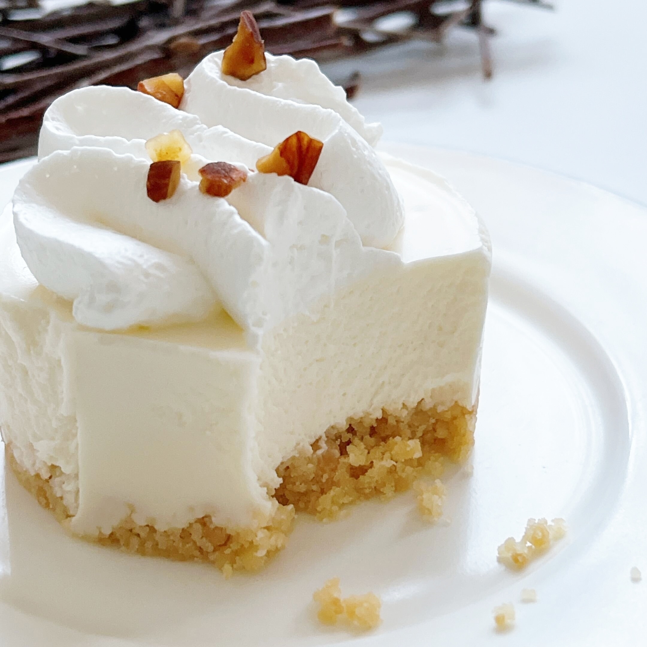 クリームとナッツがトッピングされたスライスされたチーズケーキ。皿の上に盛り付けられ、背景にはバニラビーンズが見える。