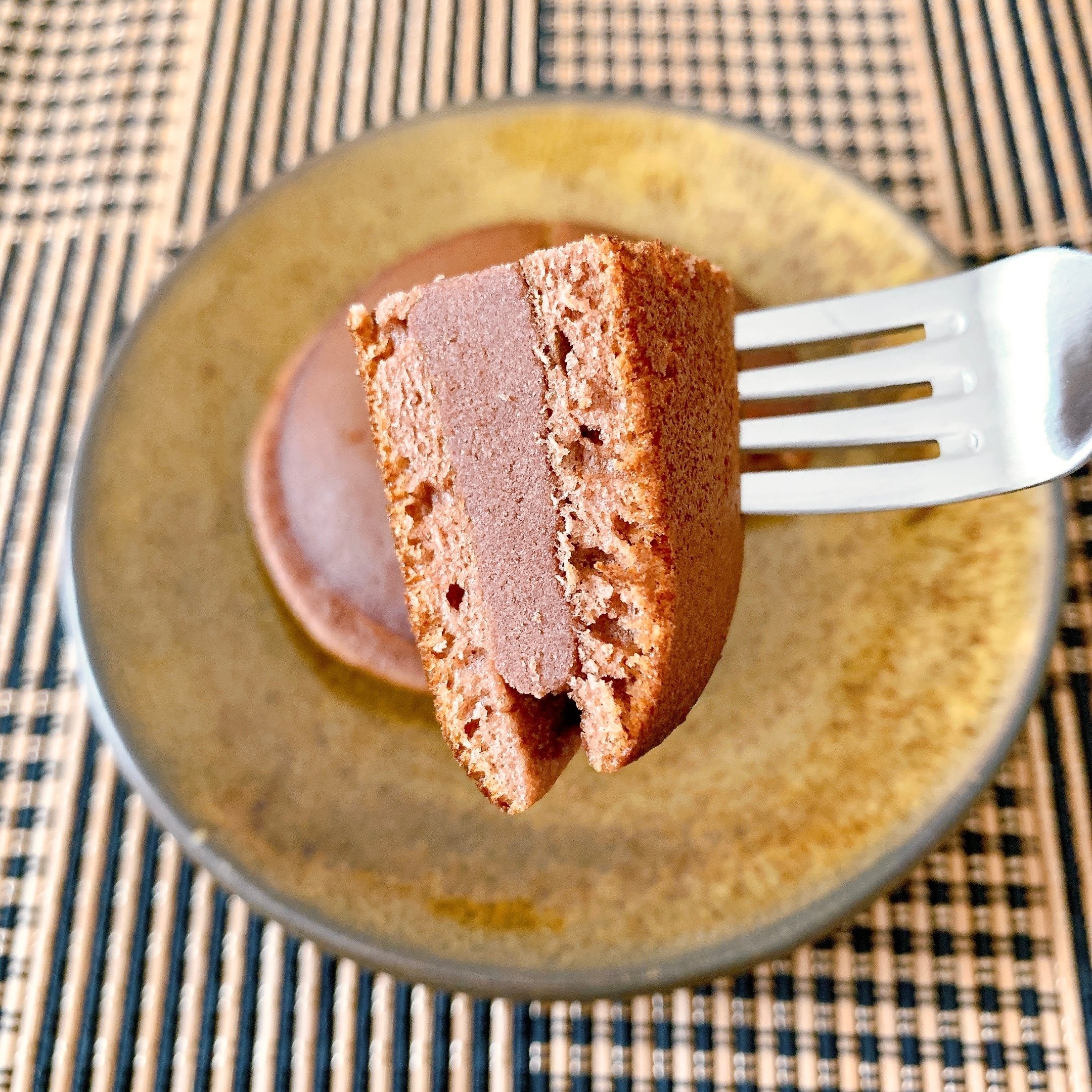 フォークに刺さったチョコレートスフレケーキの断面が見られる。板の上に置いてある。