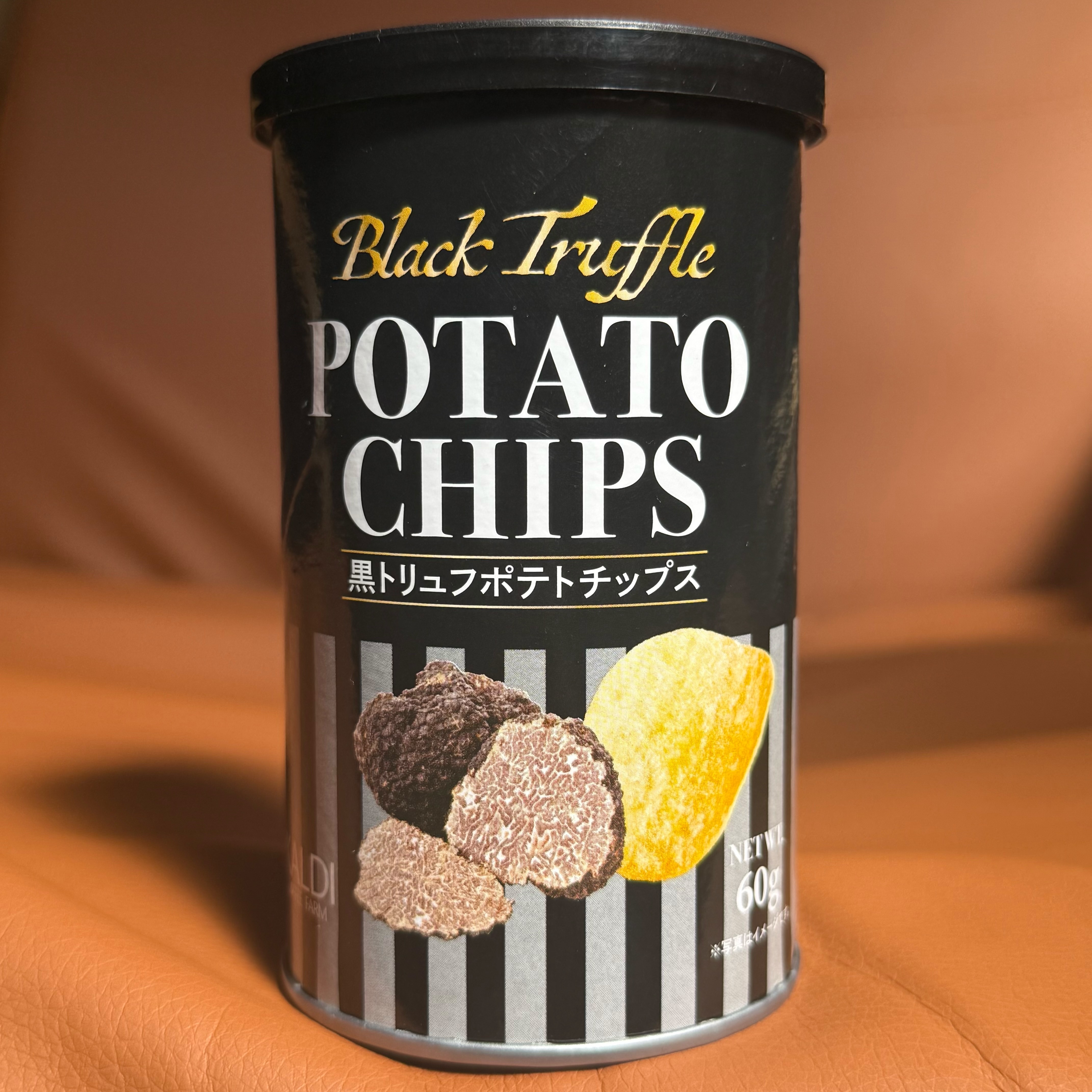 「ブラックトリュフ ポテトチップス」の缶がソファに置かれている。高級感のあるパッケージデザイン。