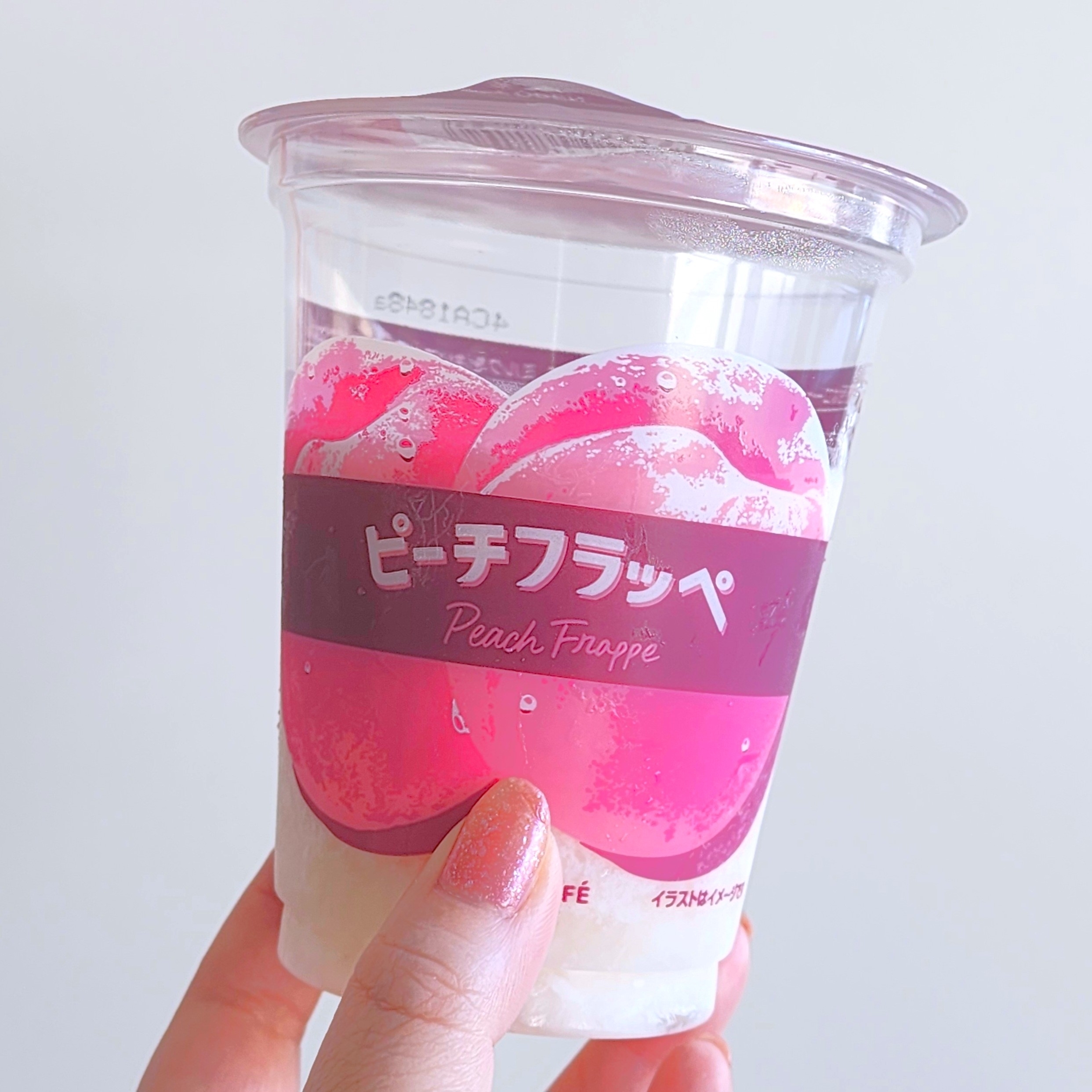 カップに入ったピーチフラッペが手で持たれています。カップには桃が描かれ、下部は白いフラッペが見えます。