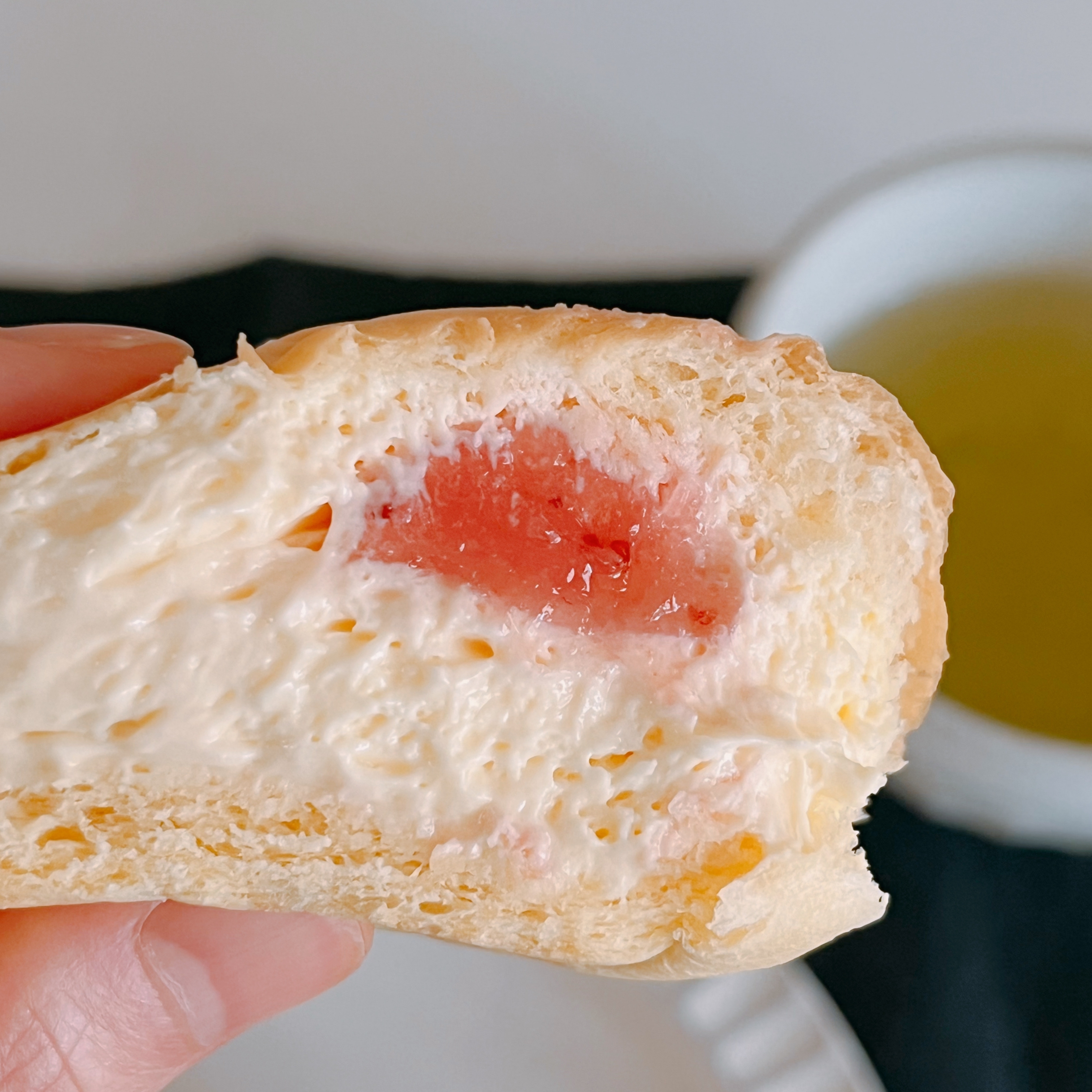 クリームとジャムが入ったパンを持つ手。背景にお茶が置かれている。