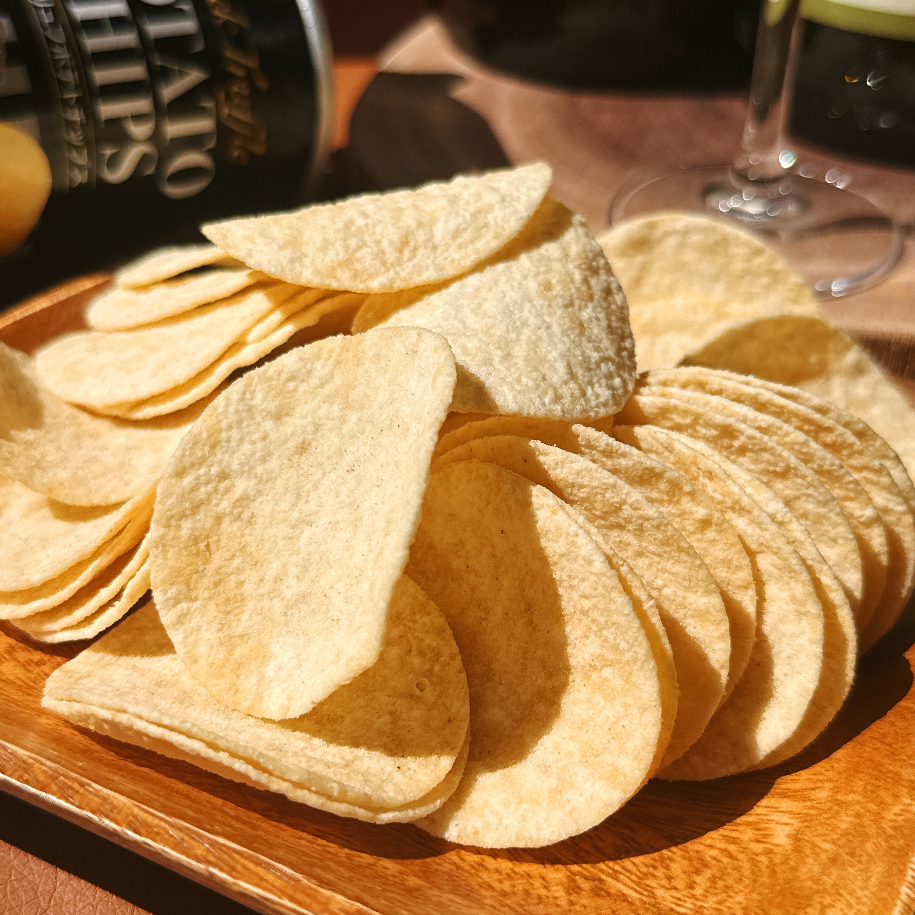 木製トレイに盛られたポテトチップスのクローズアップ。後ろに缶とグラスが見える。