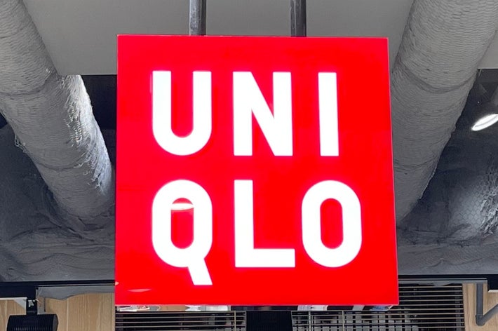 A red Uniqlo store sign hangs from the ceiling, surrounded by ventilation pipes and shelves with folded clothes