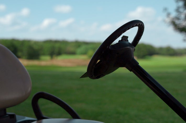 ゴルフ場と思われる場所に停まっているゴルフカートの運転席前。背景には広がる緑の芝生。