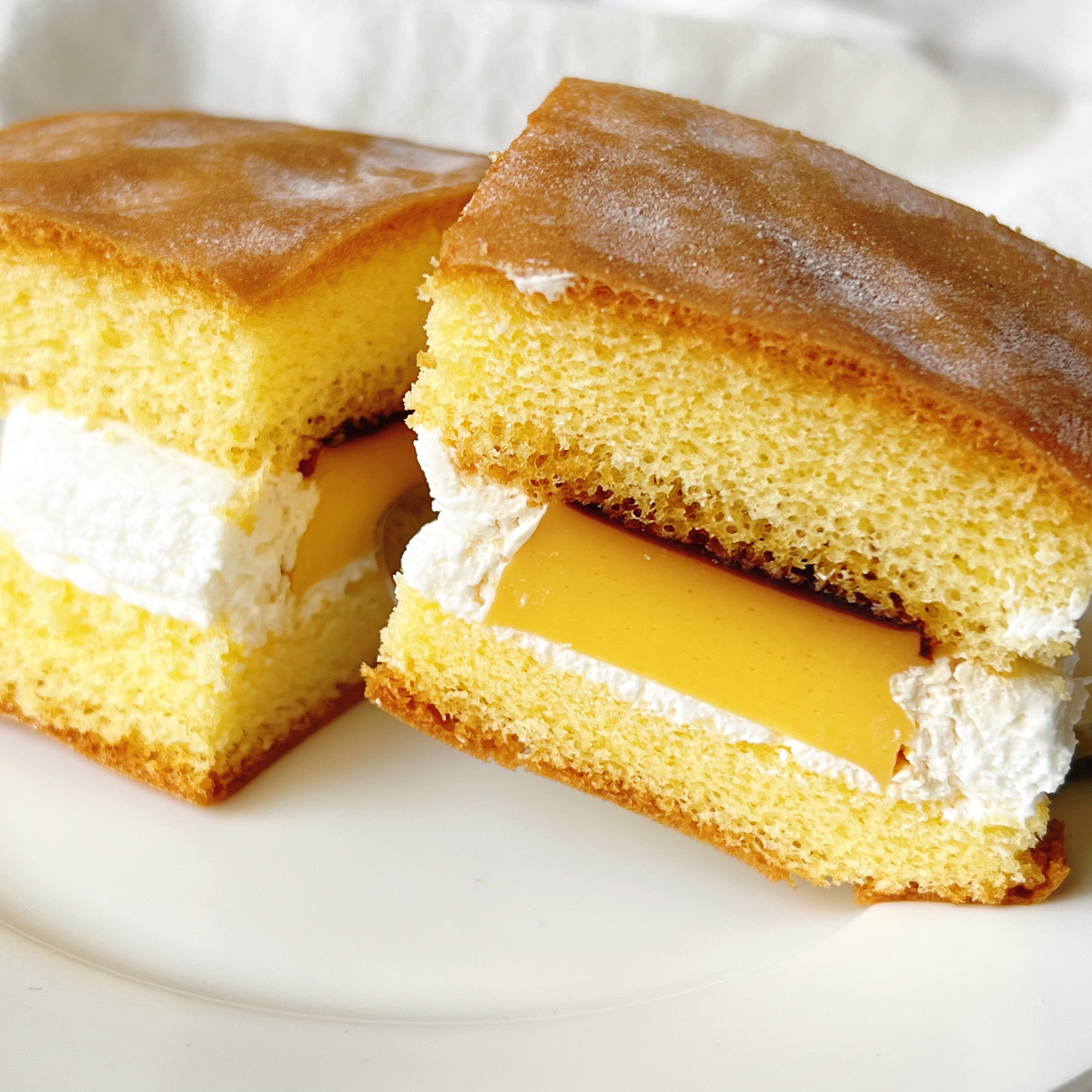 スフレケーキにクリームとカスタードがサンドされたデザートが白いお皿に乗っている。