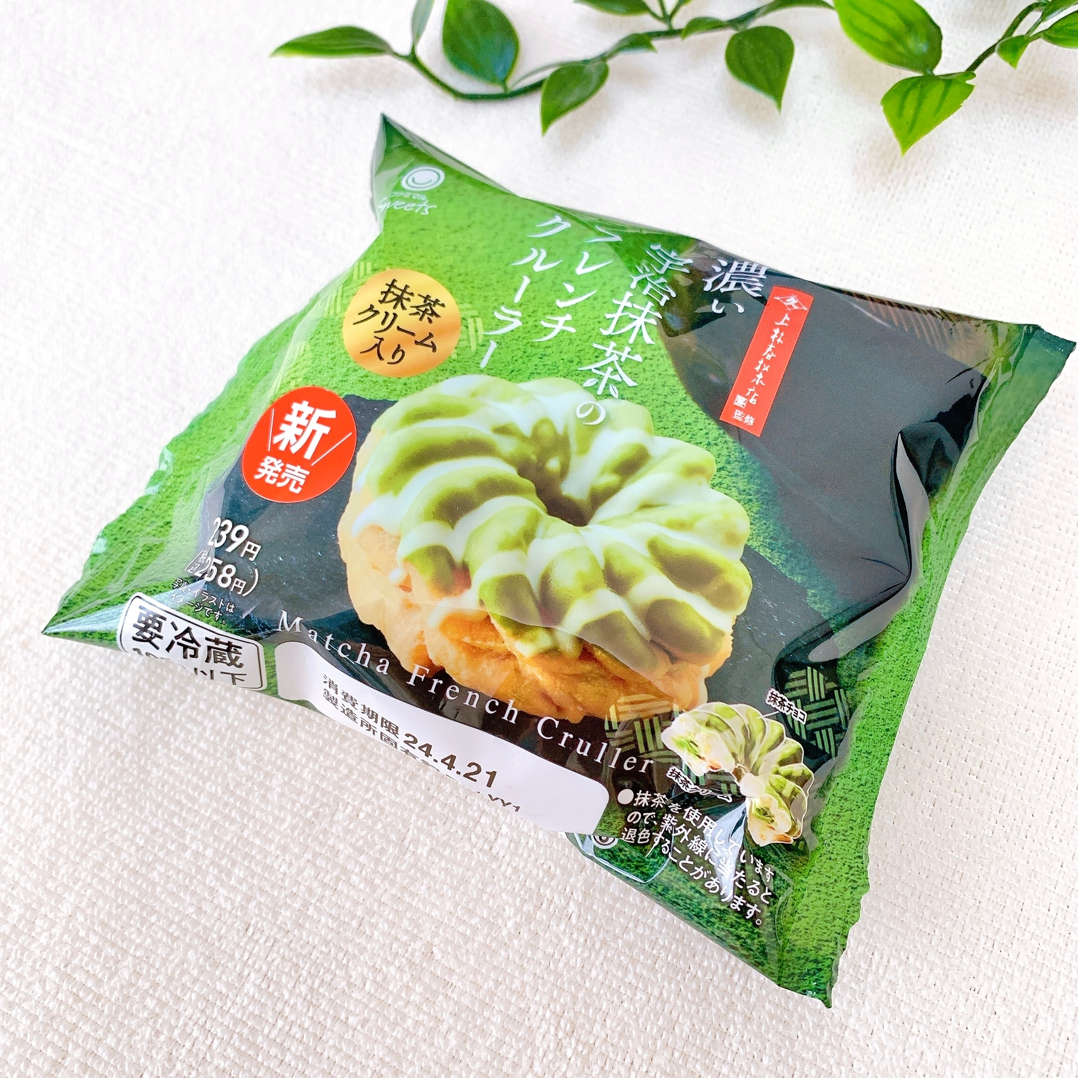 袋入りの抹茶フレンチクルーラー。新商品として発売され、抹茶クリーム入りと記載。背景に緑の葉があしらわれている。
