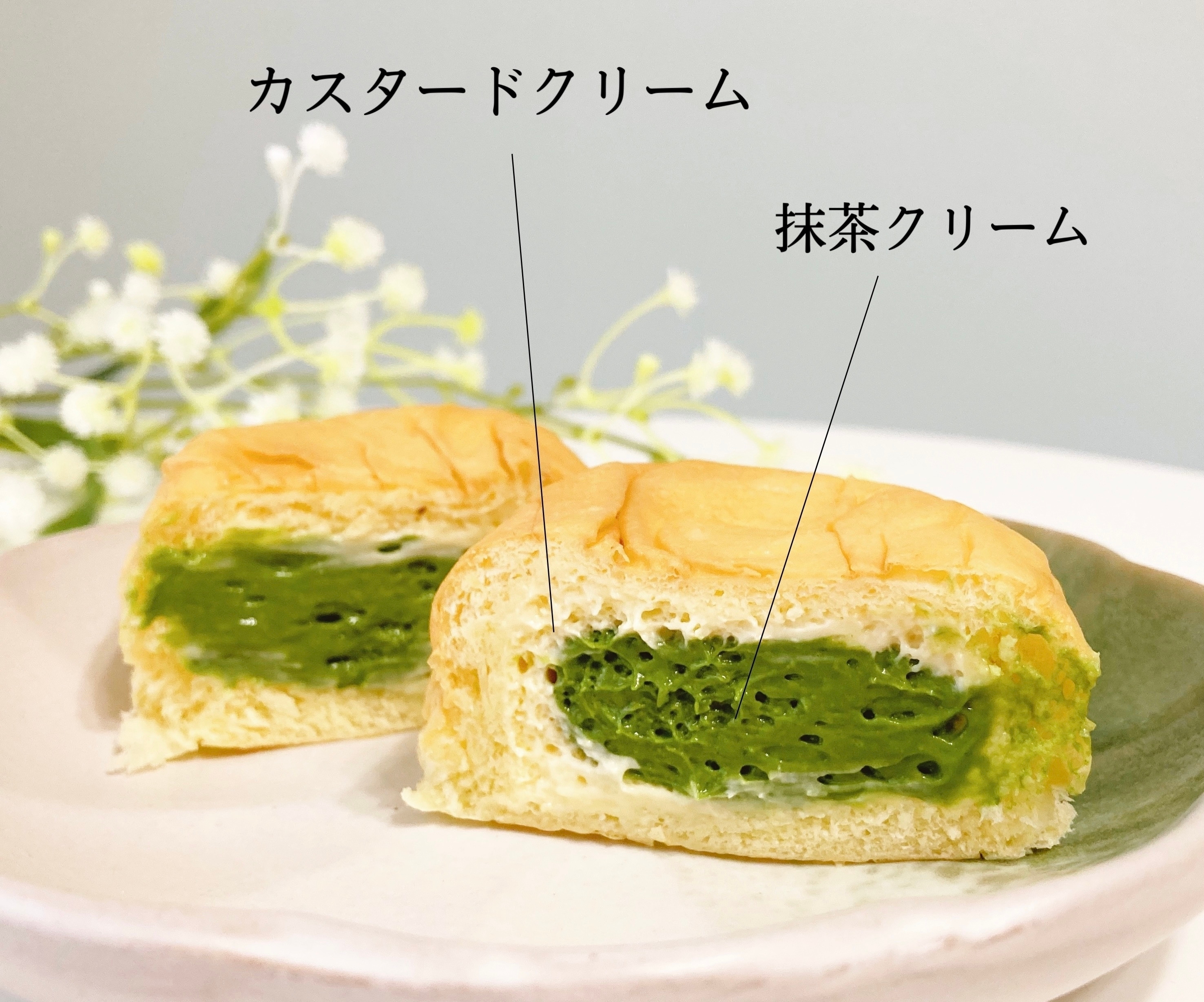 和菓子の断面。抹茶クリームとカスタードクリームが見える。背景に小さな白い花の飾り。