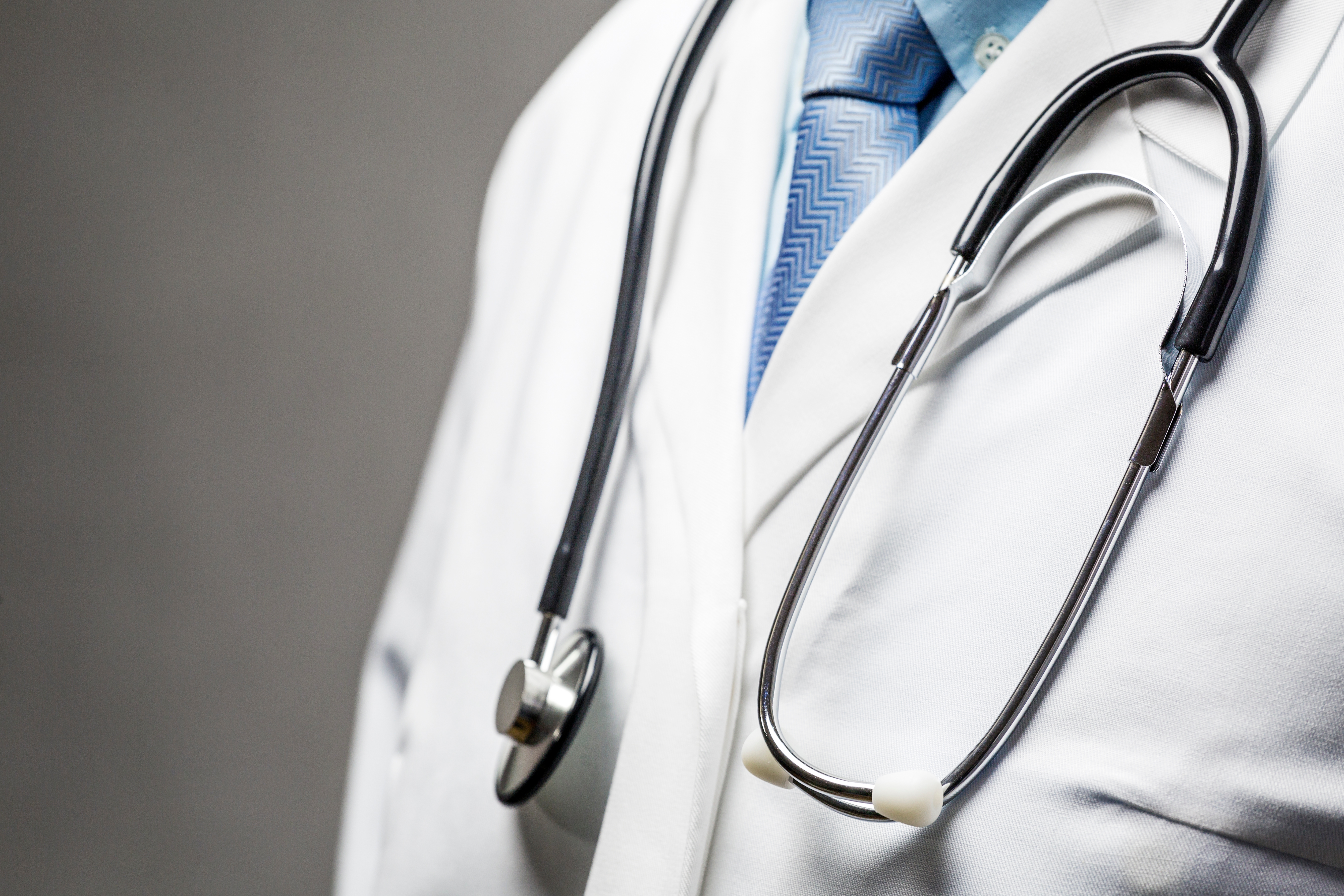 A doctor wearing a stethoscope draped over a white coat, with a tie visible underneath.