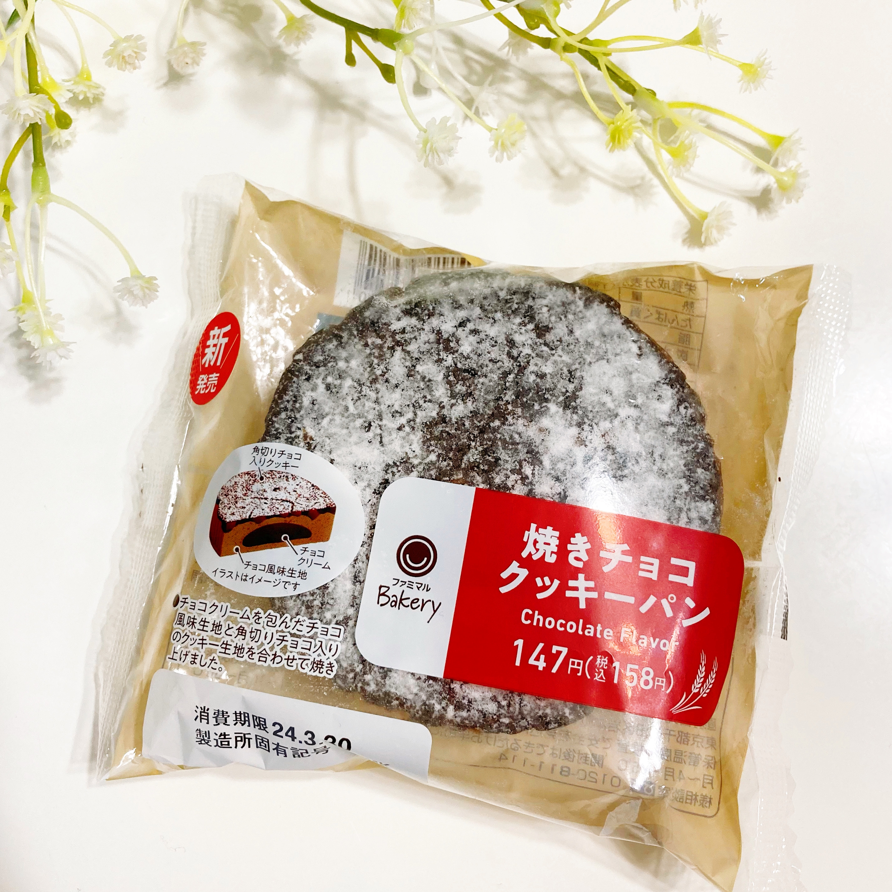 パンの包装には「焼きチョコクッキーパン」と記載されています。価格は147円。バックグラウンドに白い花があります。