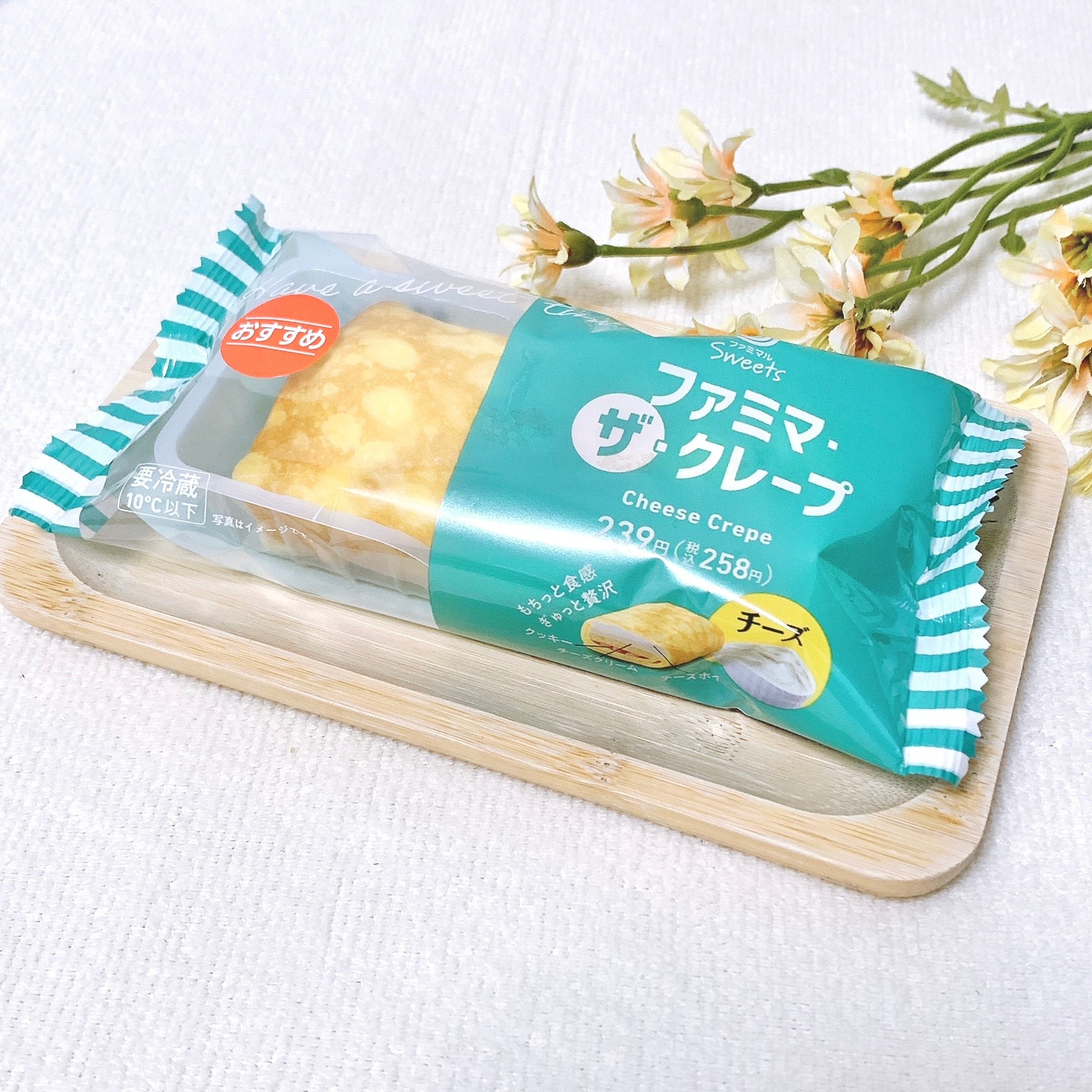 ファミリーマートのパッケージ入りチーズクレープが木製トレーにのっている。隣に花が置かれている。