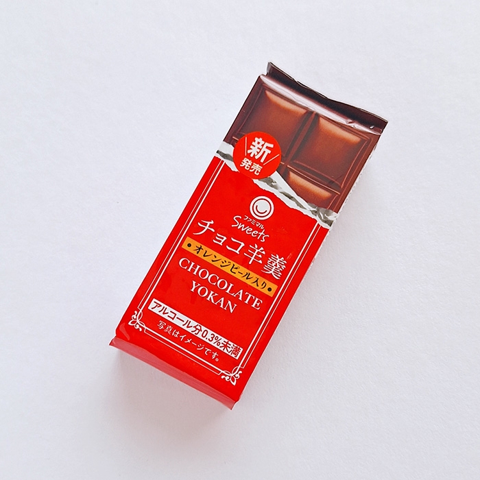 スイーツブランドの赤いパッケージに入ったチョコレート羊羹が白背景に置かれている。新商品ラベル付き。