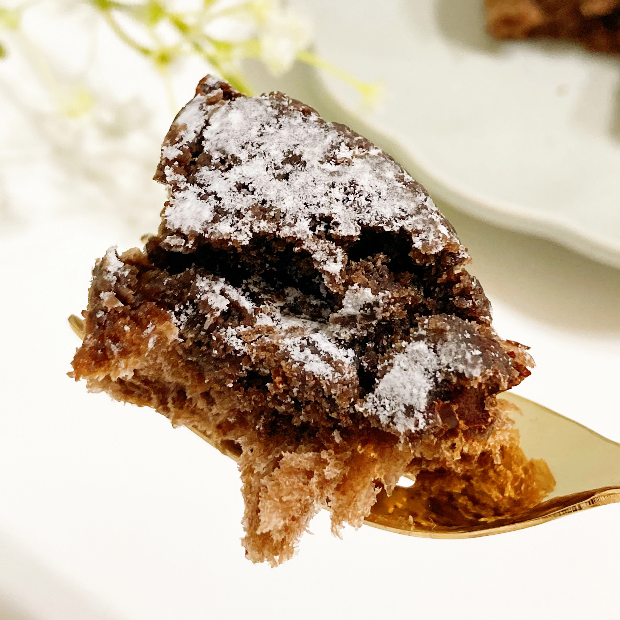 フォークに刺さった粉砂糖がふりかかったチョコレートケーキの一部。