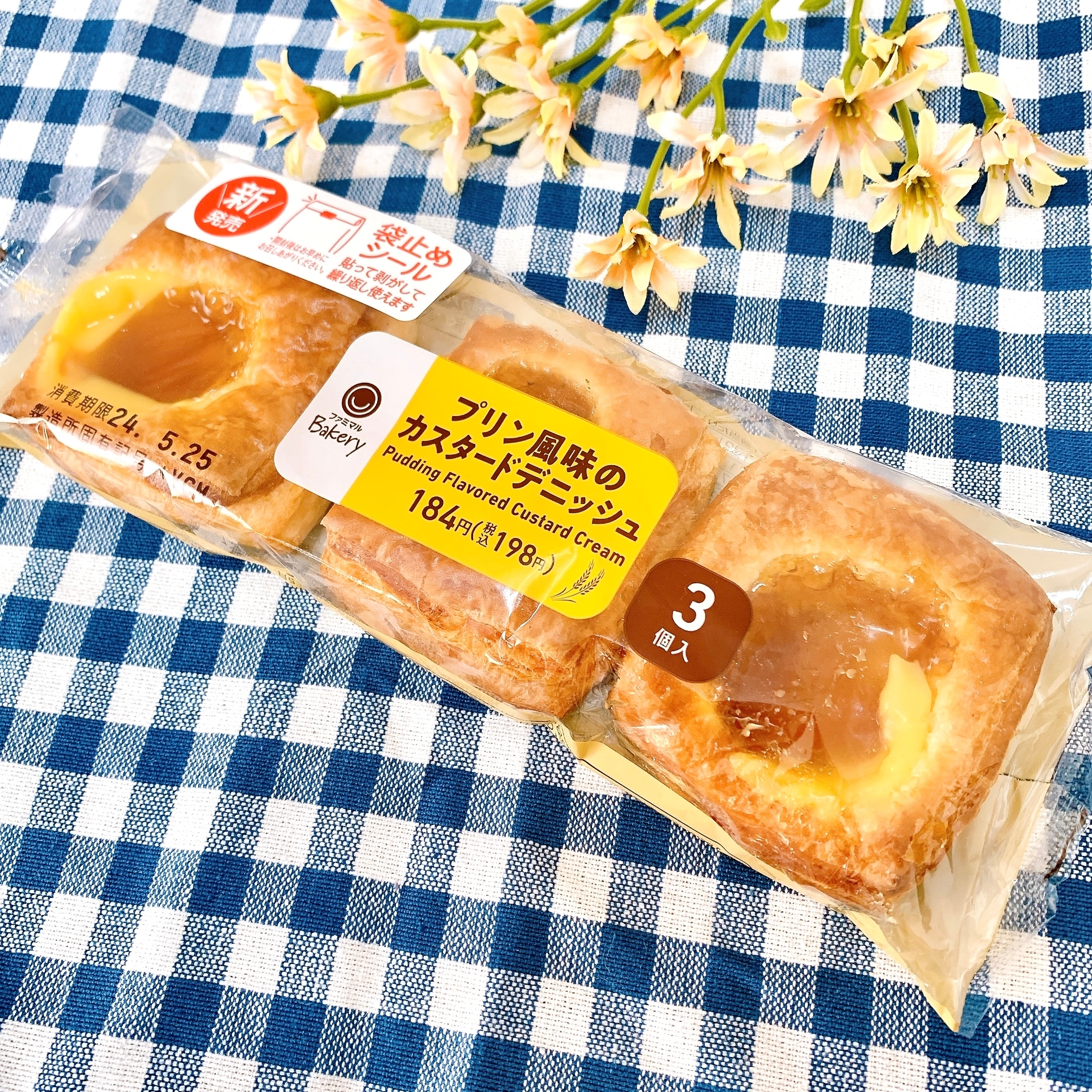 プリンクリーム風味のカスタードデニッシュ3個入りの包装。花柄の背景に置かれている。