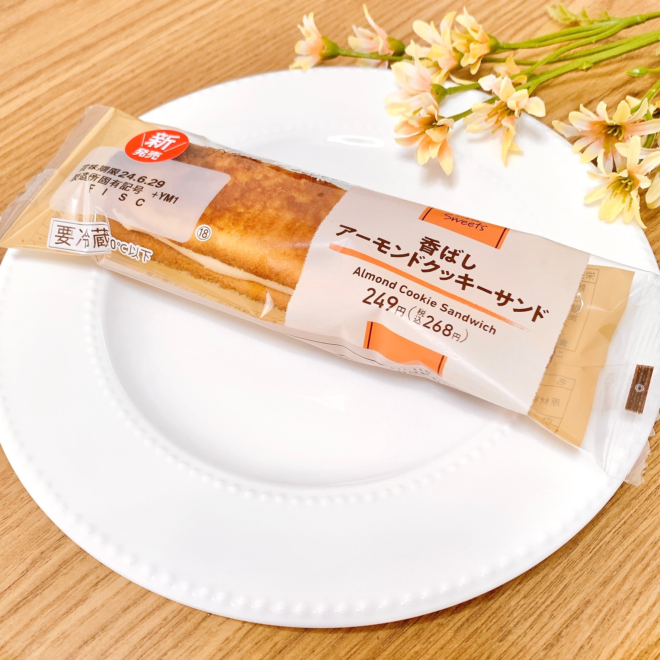 アーモンドクッキーサンドウィッチが皿に載っており、商品の包装と価格情報が表示されています。