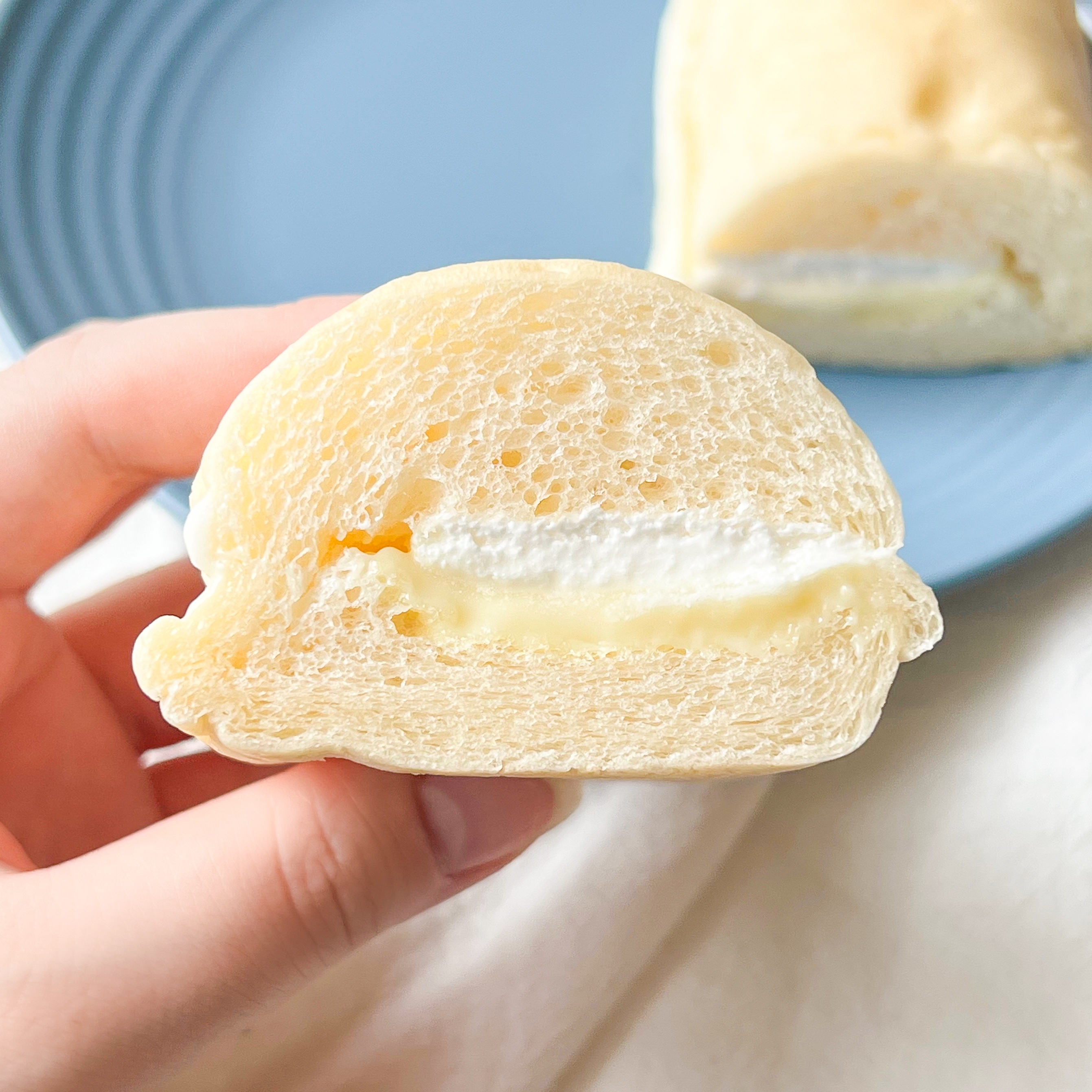 手に持たれたクリームが挟まったパン。後ろにもう一つのパンが見える。