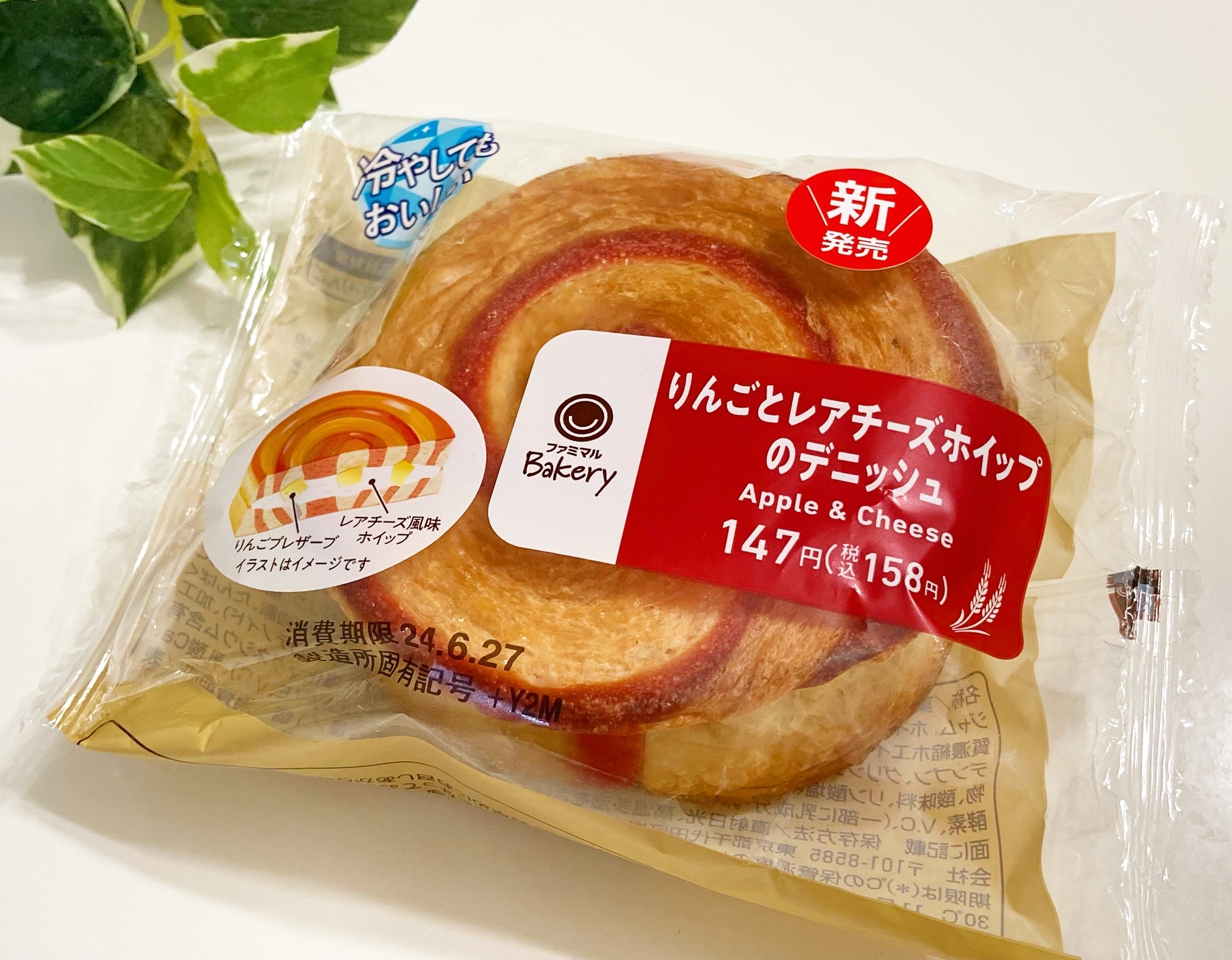 りんごとレアチーズホイップのデニッシュ。本体価格147円(税込158円)。植物の横に置かれた状態の包装デザイン。