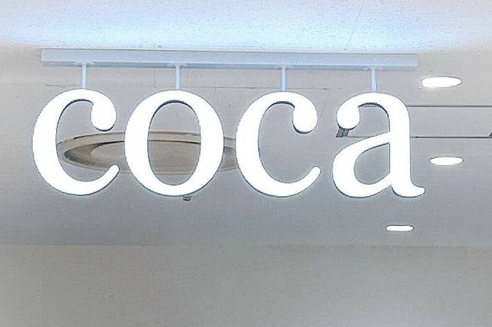 洋服店「coca」の店内サイン。背景には服が並ぶ。