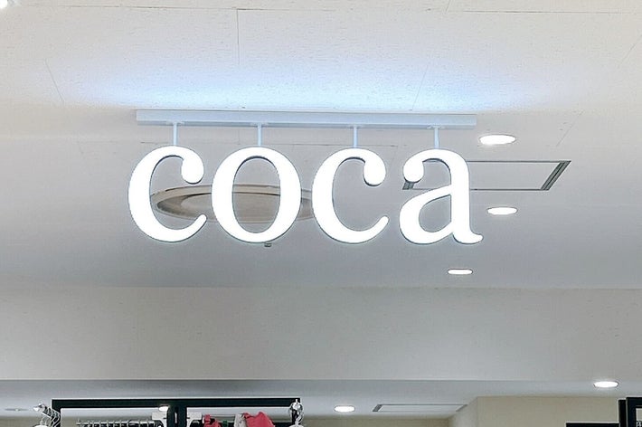 洋服店「coca」の店内サイン。背景には服が並ぶ。
