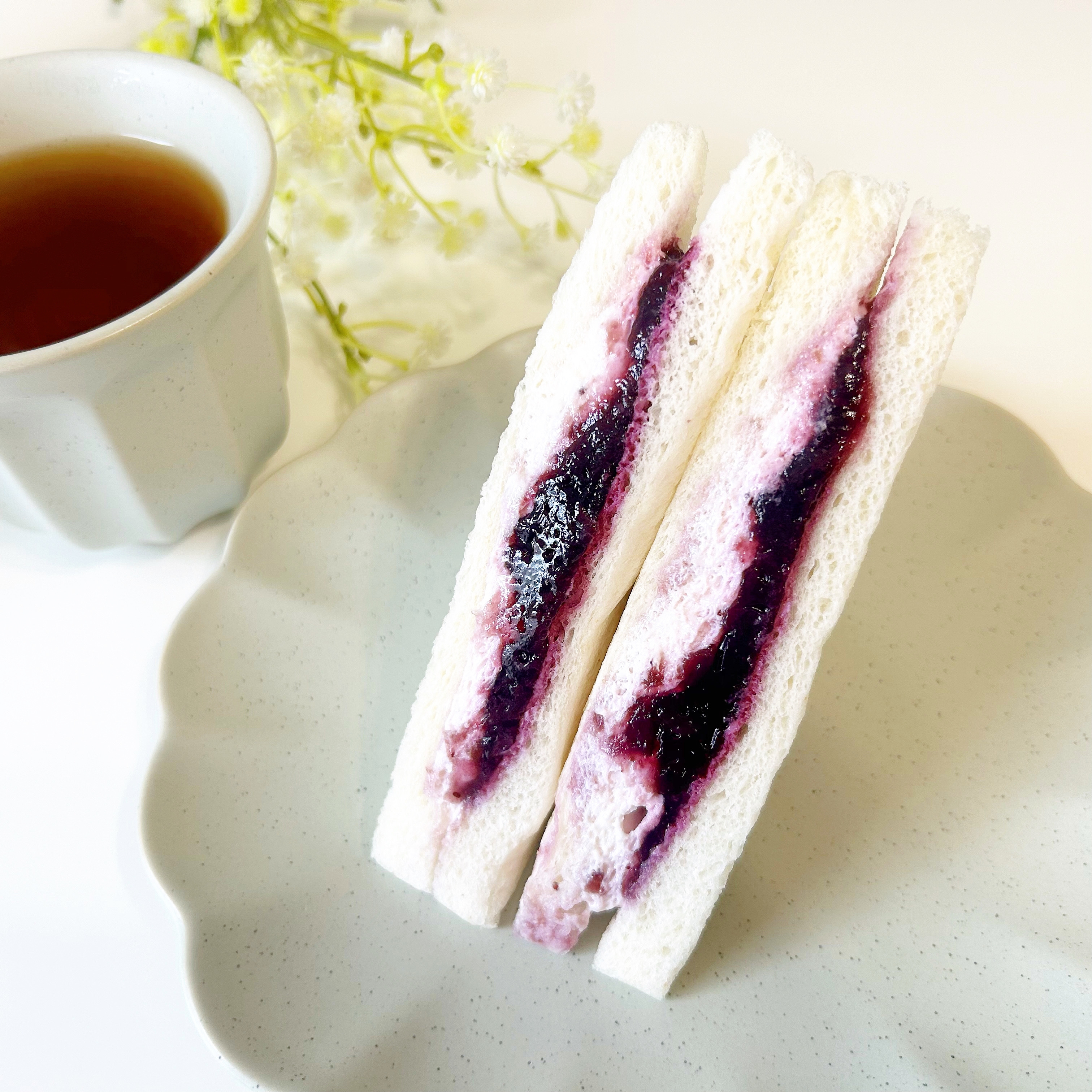 ティーセットの隣にジャムサンドが白い皿に置かれた食事のシーン。
