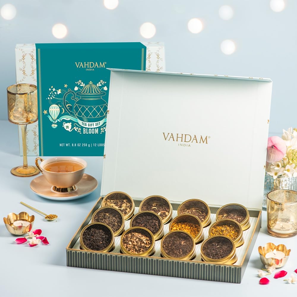 Vahdam tea gift set displayed with open box showing an assortment of teas. A teacup, saucer, and decorative elements are arranged alongside