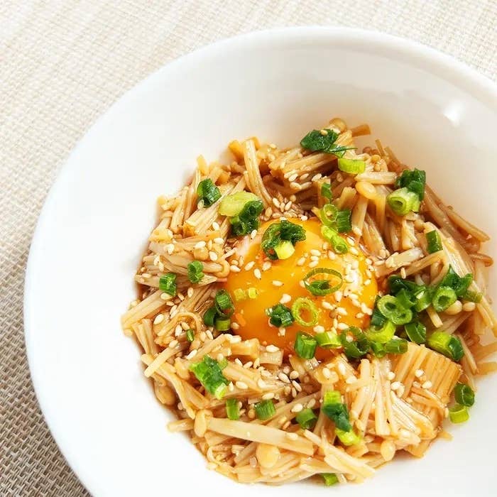 白いボウルに盛られたエノキと卵黄、上にはごまやネギがトッピングされています。