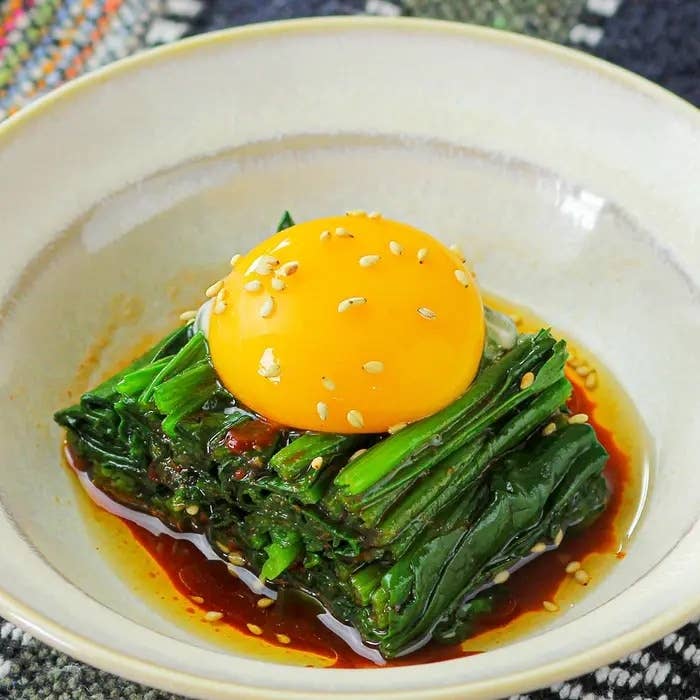 皿にほうれん草のおひたしが盛られ、その上に卵黄とごまがトッピングされている料理。