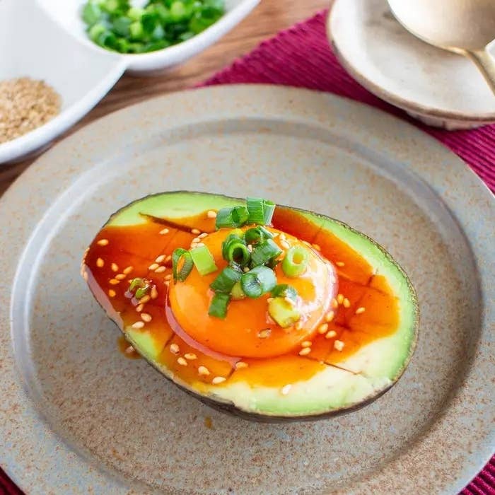 半分に切ったアボカドの上に卵黄とネギ、ソースがかかっています。お皿に盛られた料理。