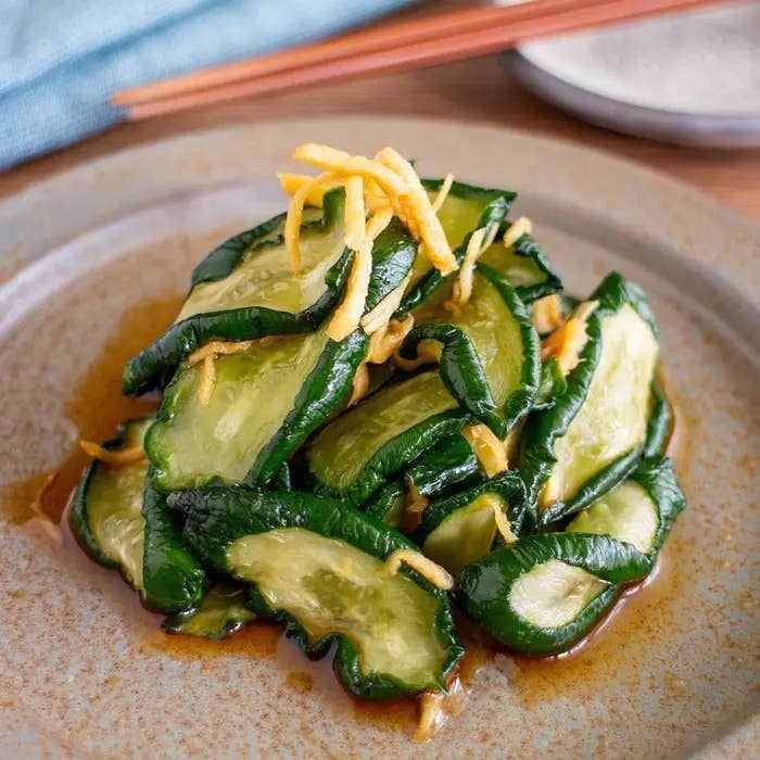 きゅうりの薄切りが盛られた皿。ドレッシングと細切りの皮が添えられている。