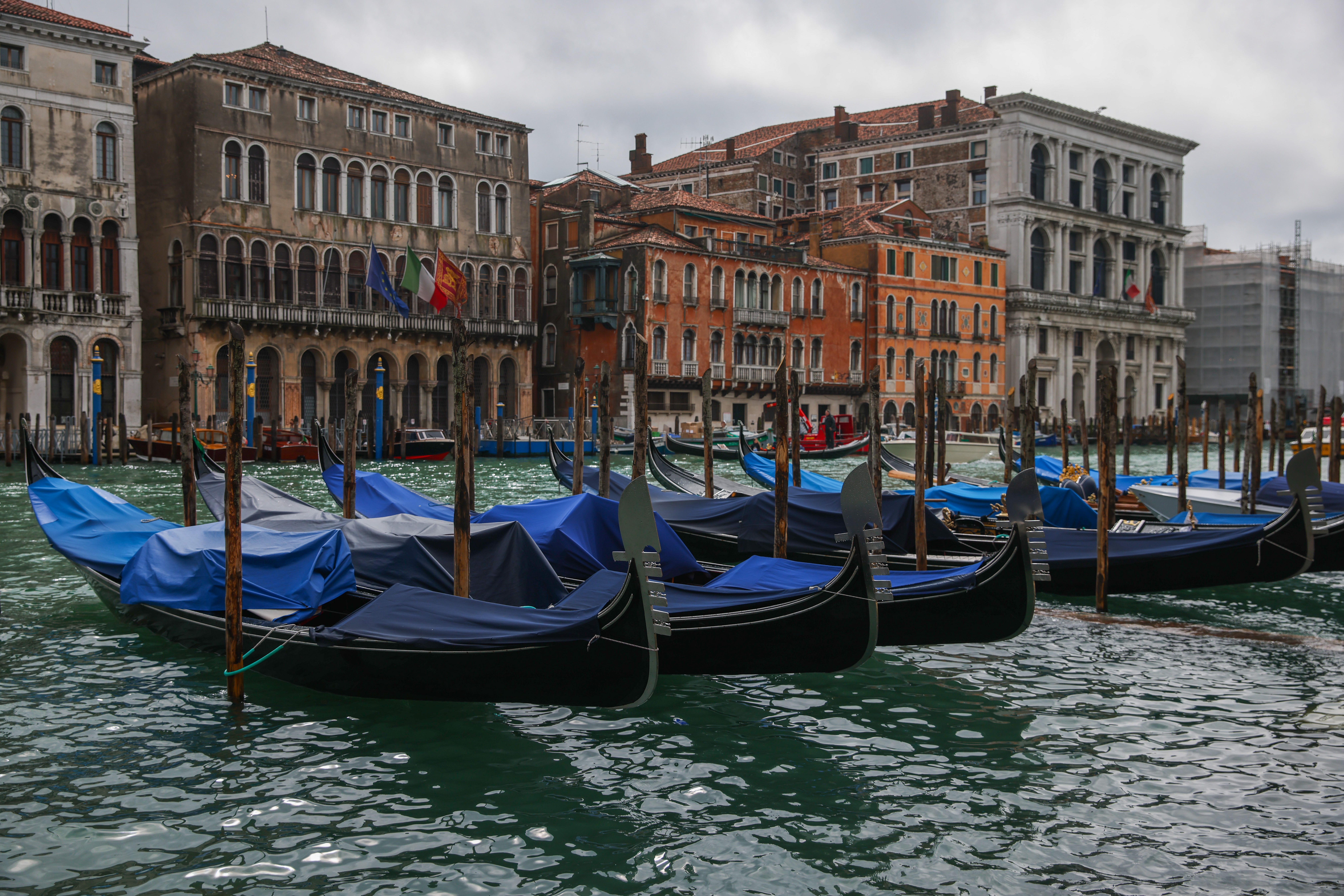 Gondolas with tarps moored along a canal in Venice, Italy, with historic buildings in the background