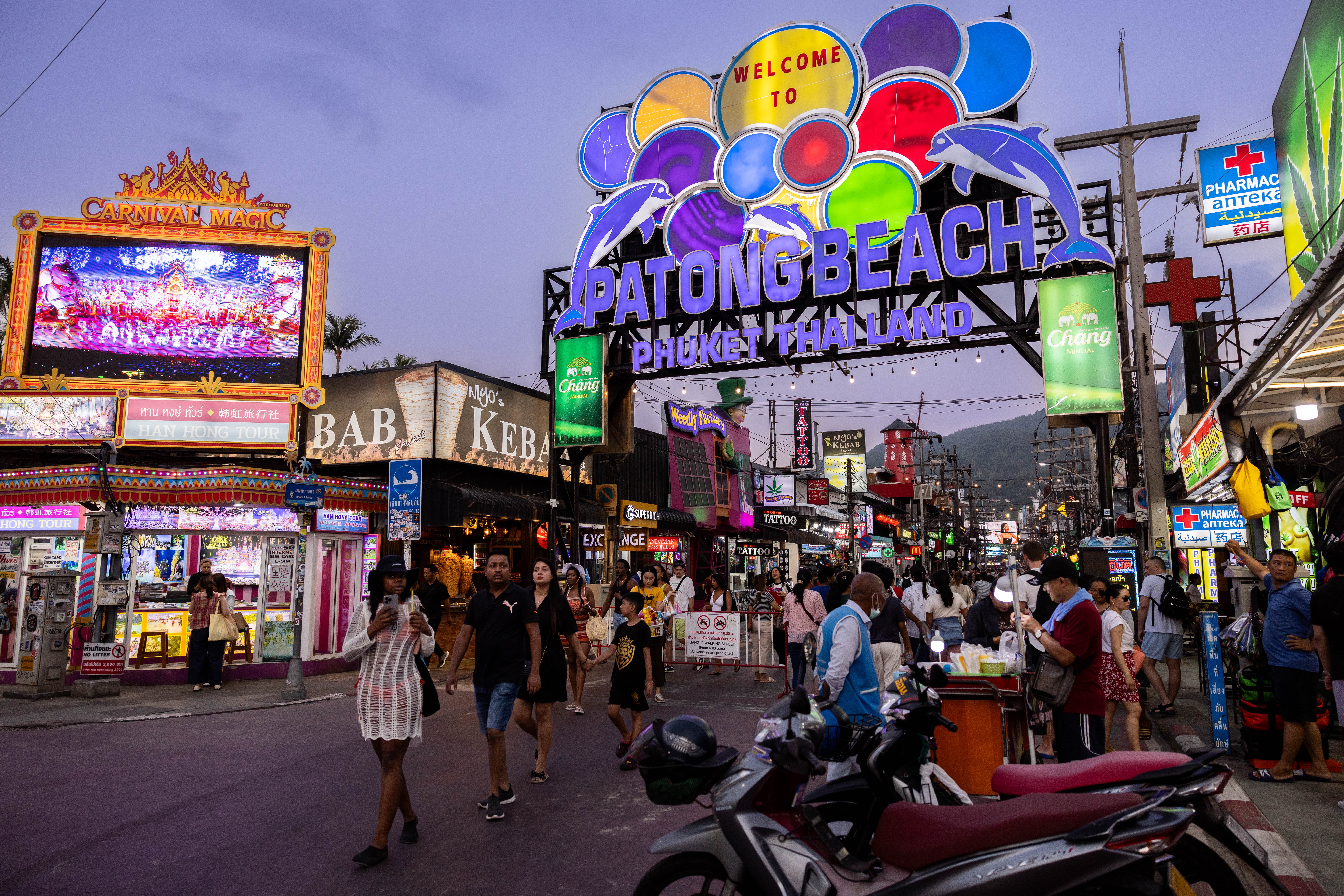Busy street scene at Patong Beach entrance, with neon signs, pedestrians, and various shops creating a lively, bustling atmosphere