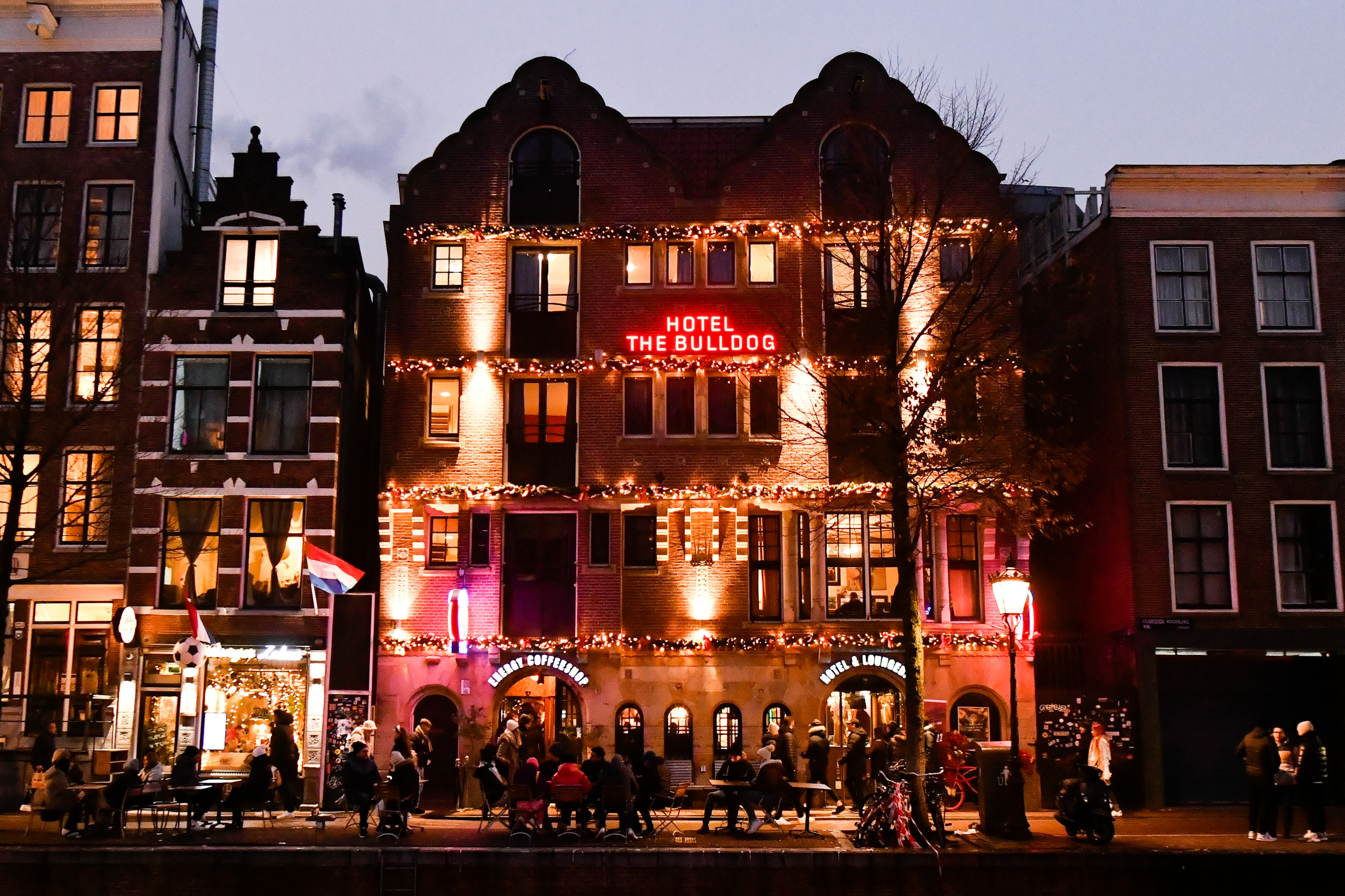 Street scene with people walking by Hotel The Bulldog, a lit-up building with festive decorations at night