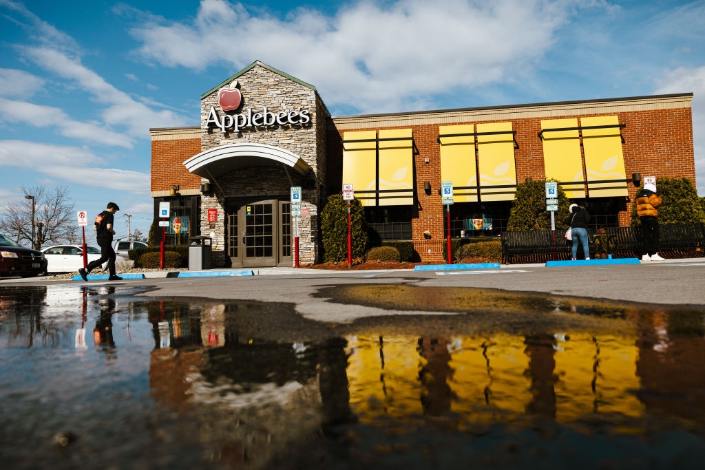 Applebee's restaurant exterior with people walking in the parking lot, reflecting in a large puddle