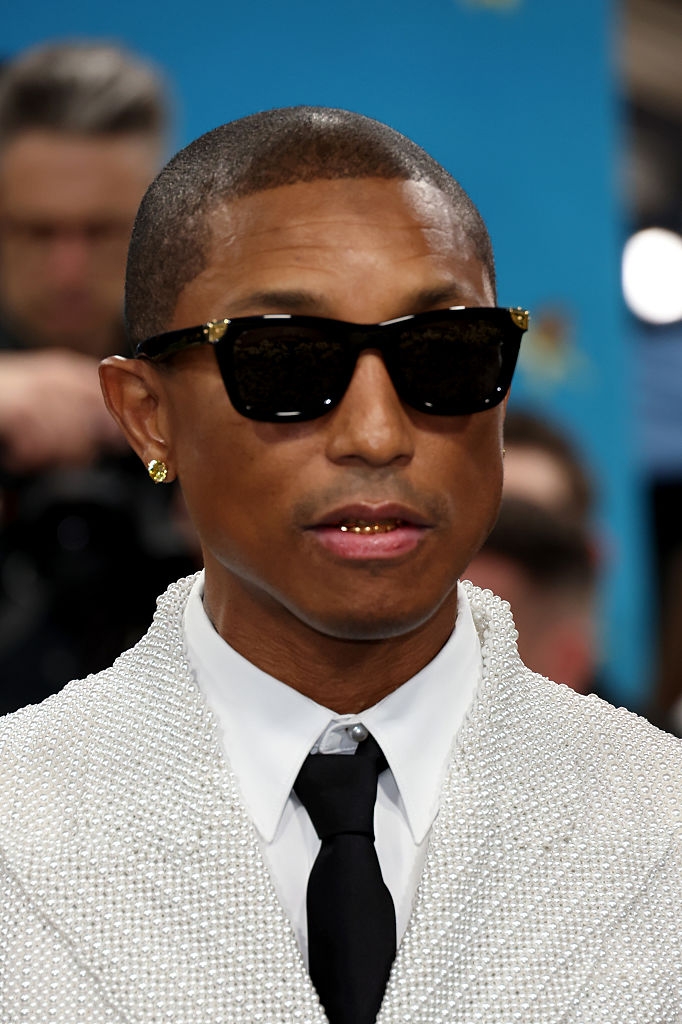 A person in a beaded blazer and tie, wearing sunglasses and a gold grill, attends a celebrity event